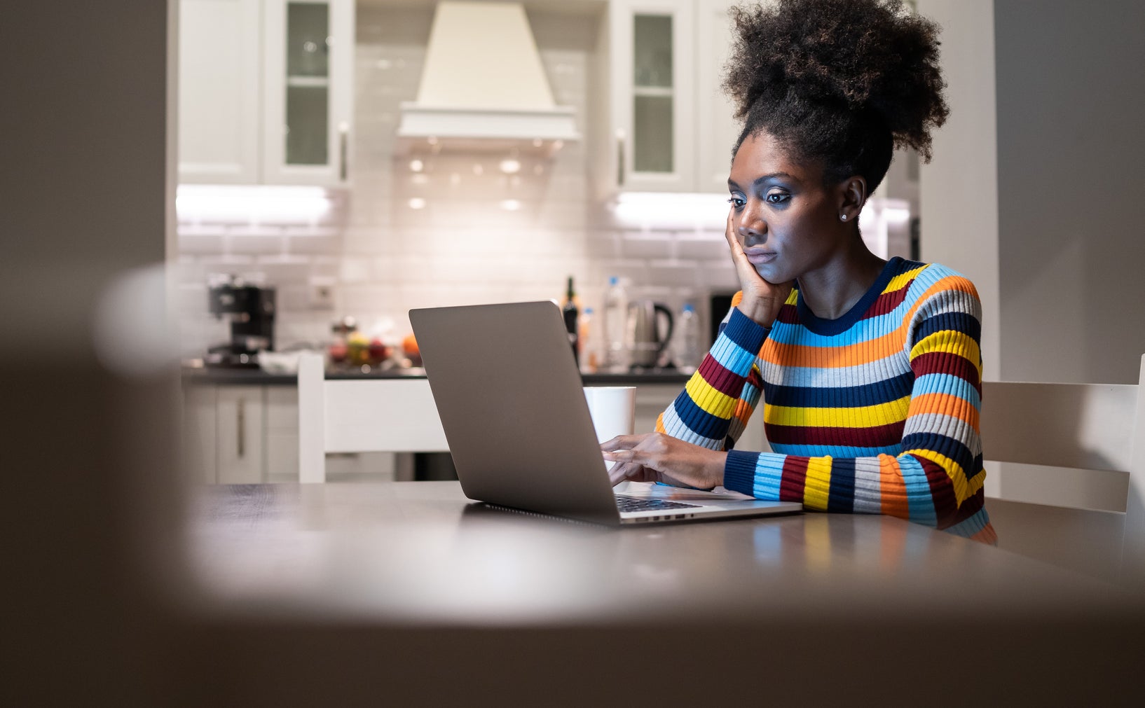 Woman in striped top works on laptop in a home kitchen, focused on screen