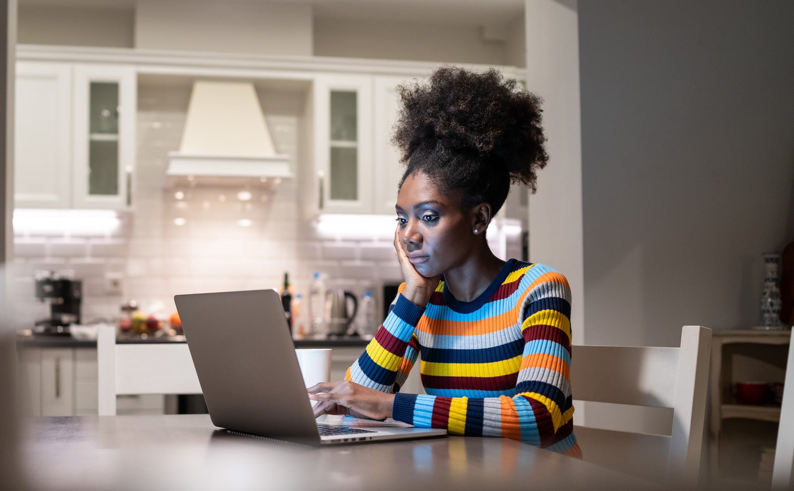 Woman in striped top works on laptop in a home kitchen, focused on screen