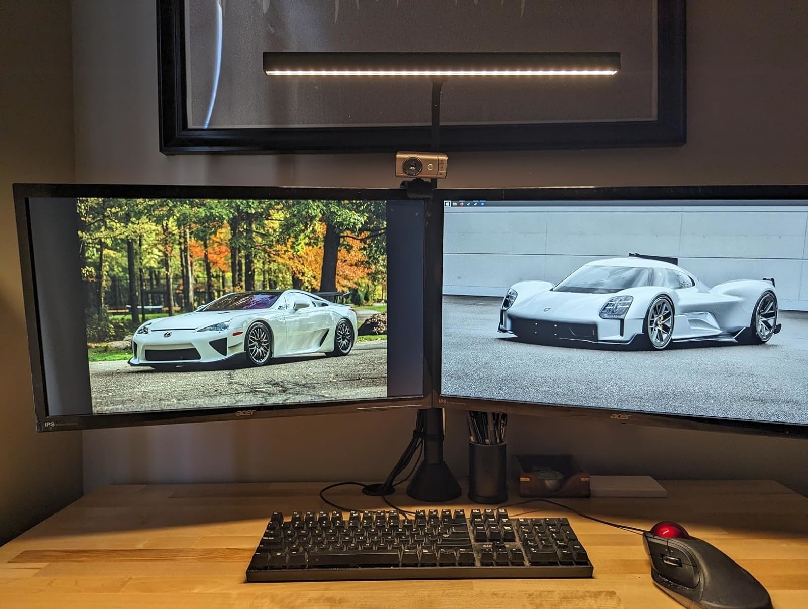 Dual monitors displaying sports cars, one in nature and one in a showroom, on a desk with a keyboard and mouse
