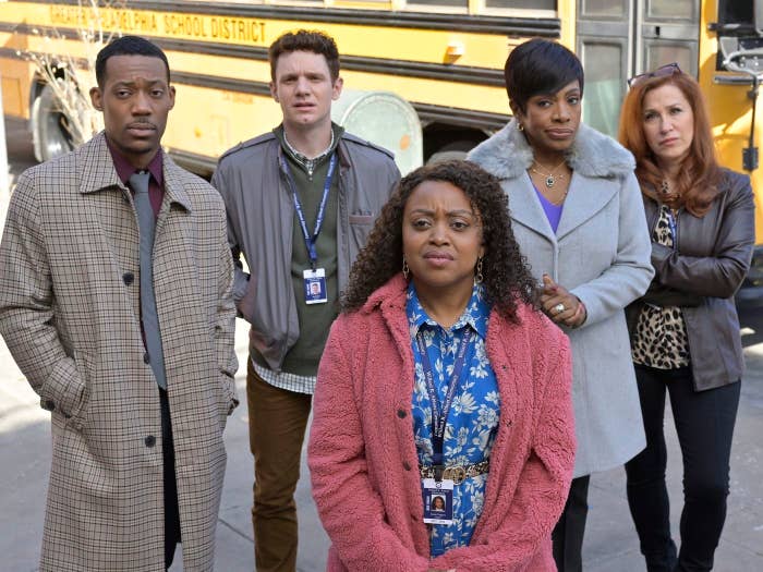 Four actors from a TV show stand in front of a school bus; two women and two men, dressed in winter clothes