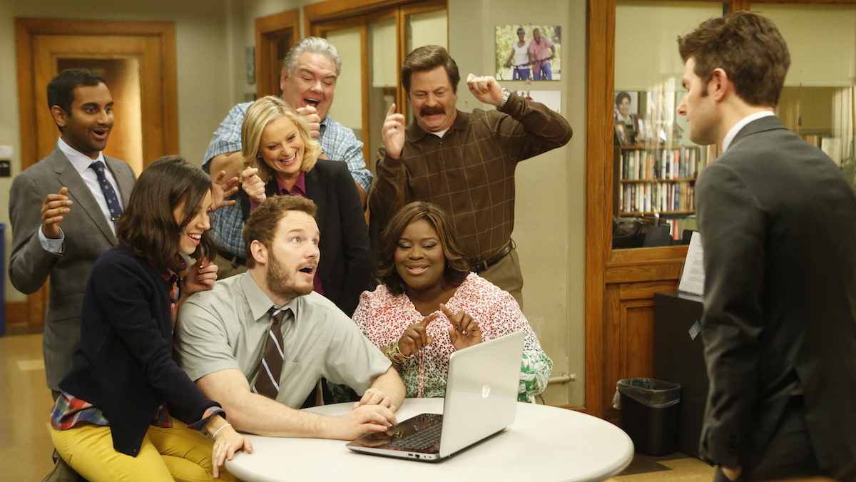 Cast of &quot;Parks and Recreation&quot; excitedly gathered around a laptop with a person standing across from them