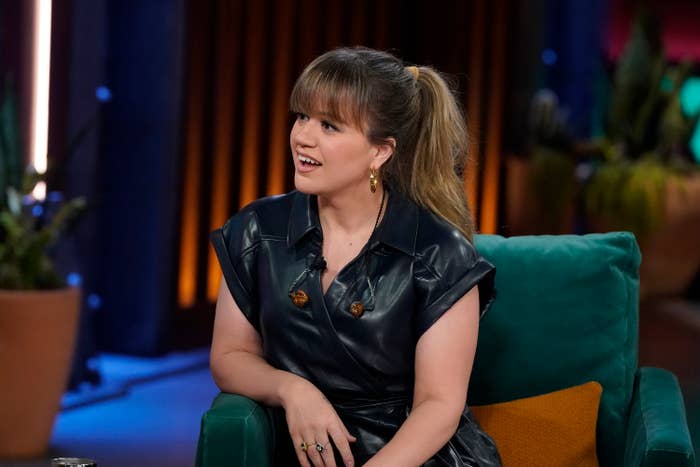 Kelly wearing a leather outfit and sitting on a talk show set