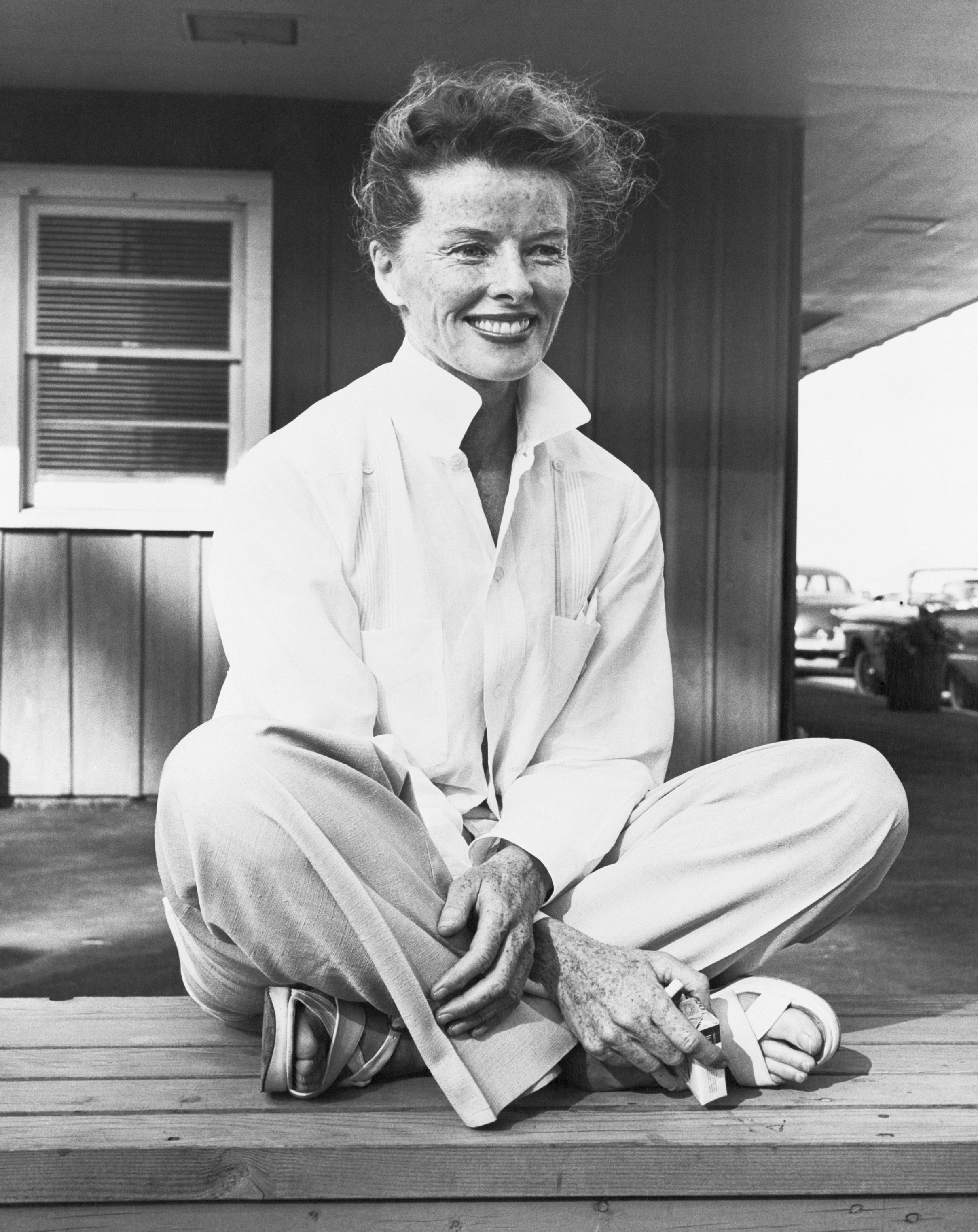 Woman in a buttoned shirt and slacks sitting cross-legged with a smile
