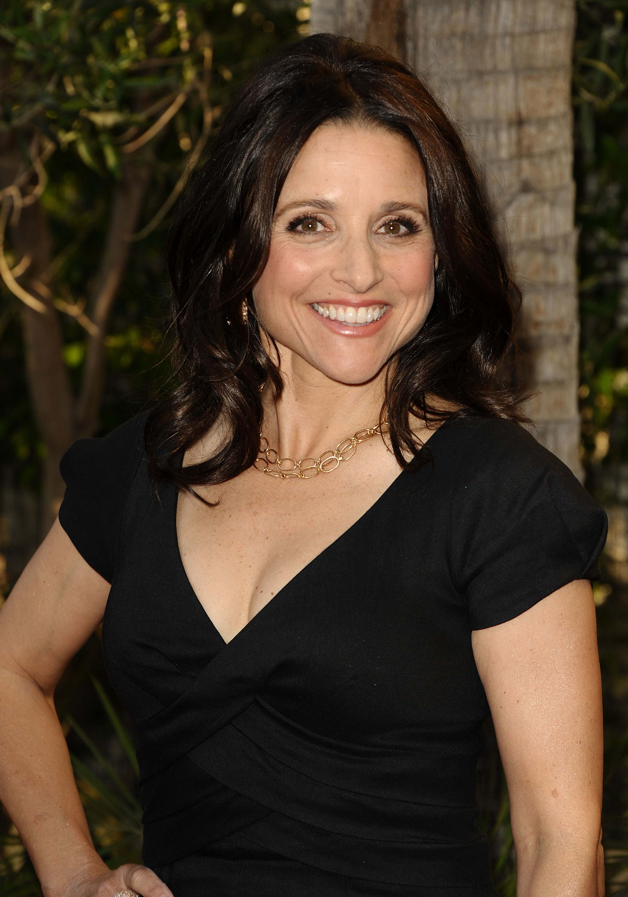 Smiling woman with medium-length hair in a V-neck black dress and gold necklace