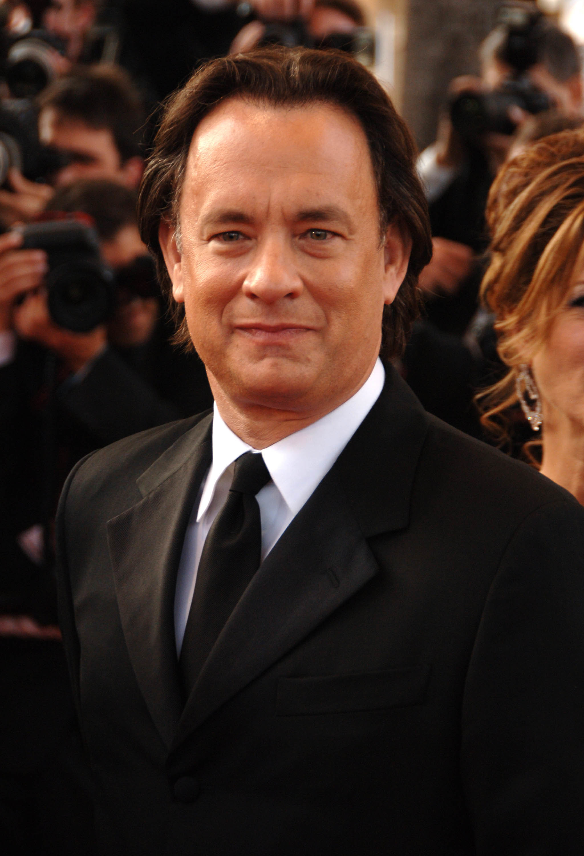 Tom Hanks in a classic black tie attire at an event, looking directly at the camera