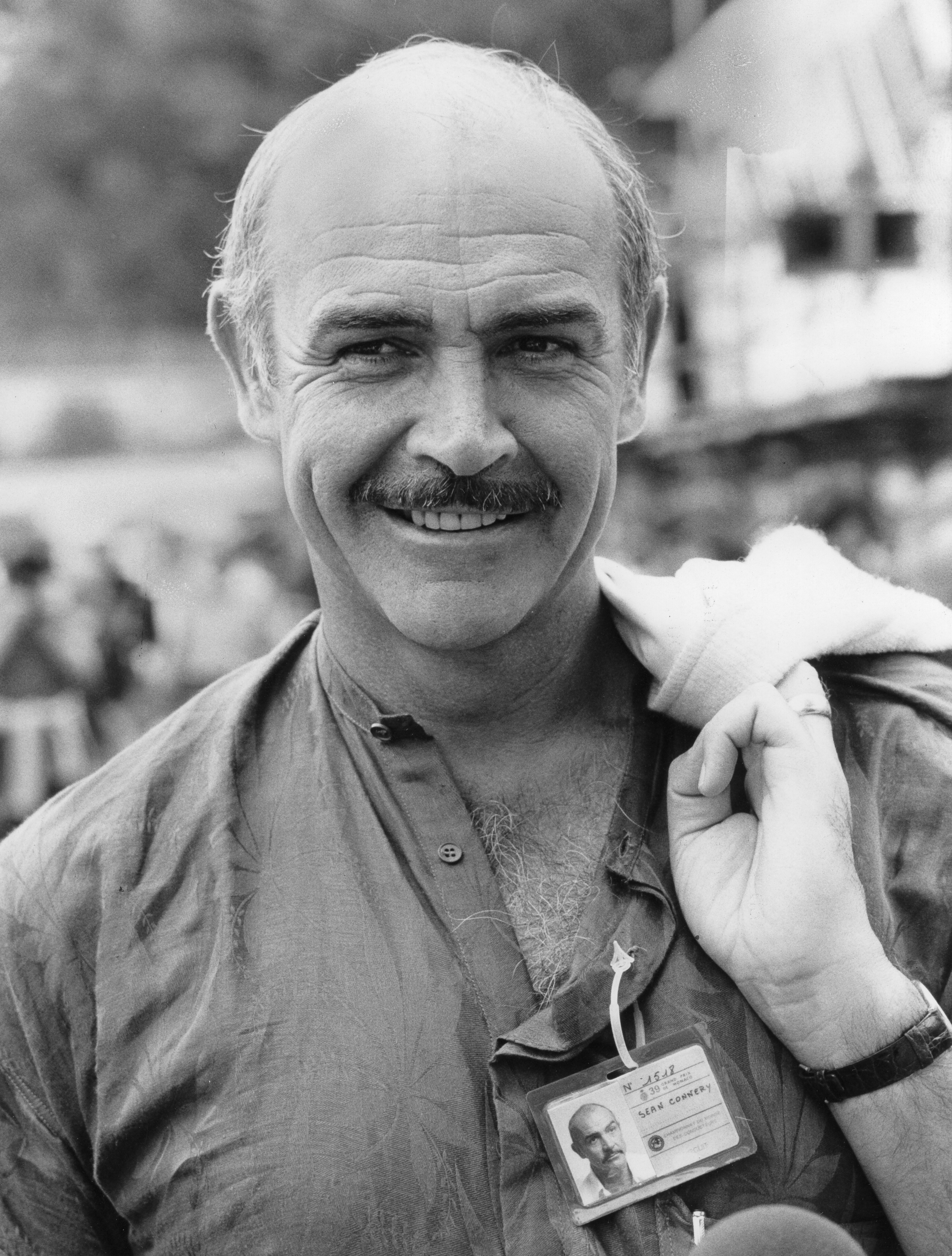 Sean Connery in a casual shirt with ID badge, smiling with a small towel over his shoulder