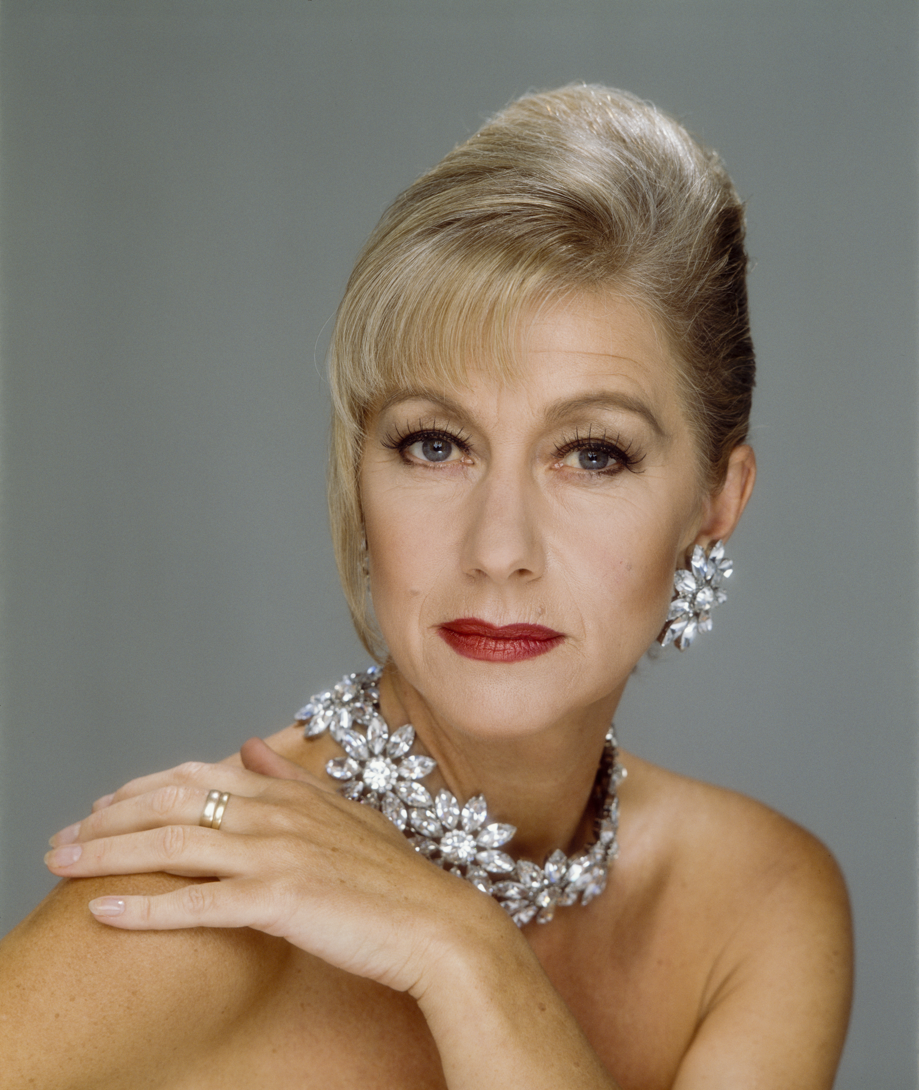 Portrait of an elegant woman with statement earrings and necklace, posing with hand on shoulder