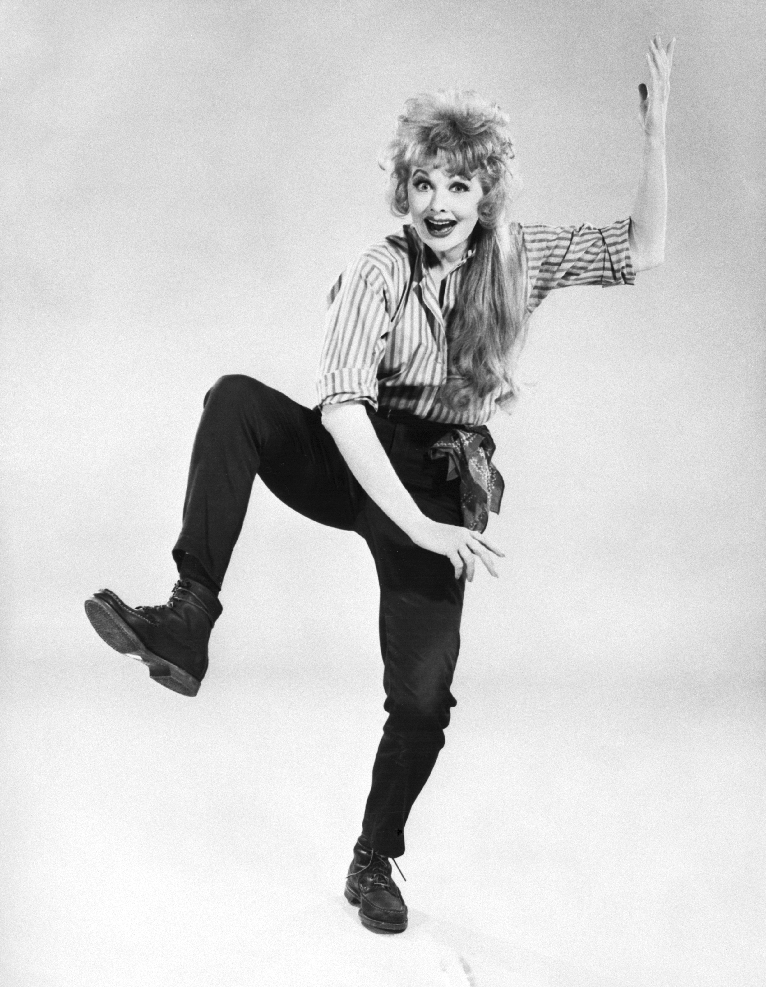 A person posing dynamically with one arm raised, wearing striped top, black pants, and boots