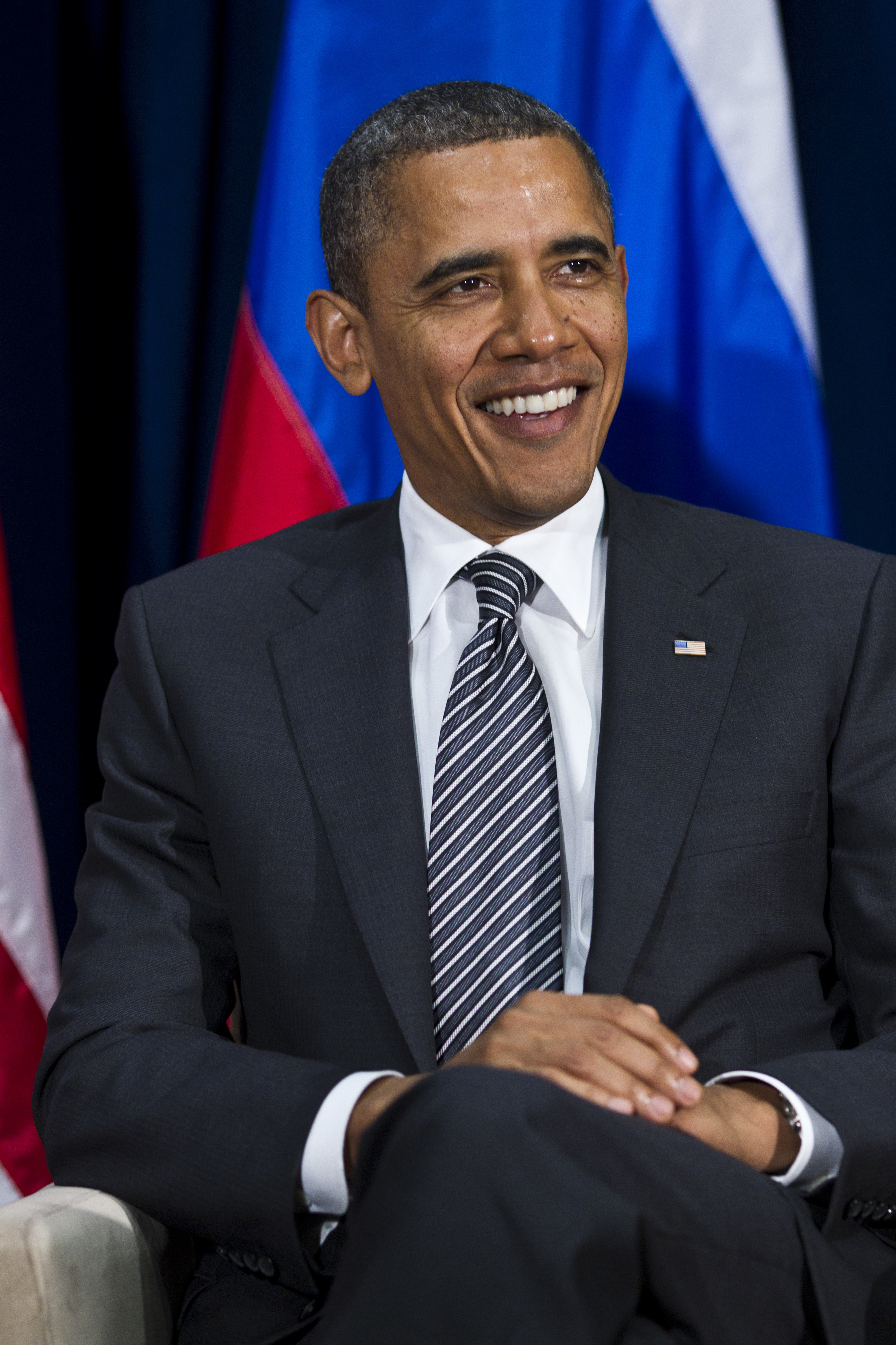 Barack Obama smiling, seated in a dark suit, white shirt, and diagonally striped tie