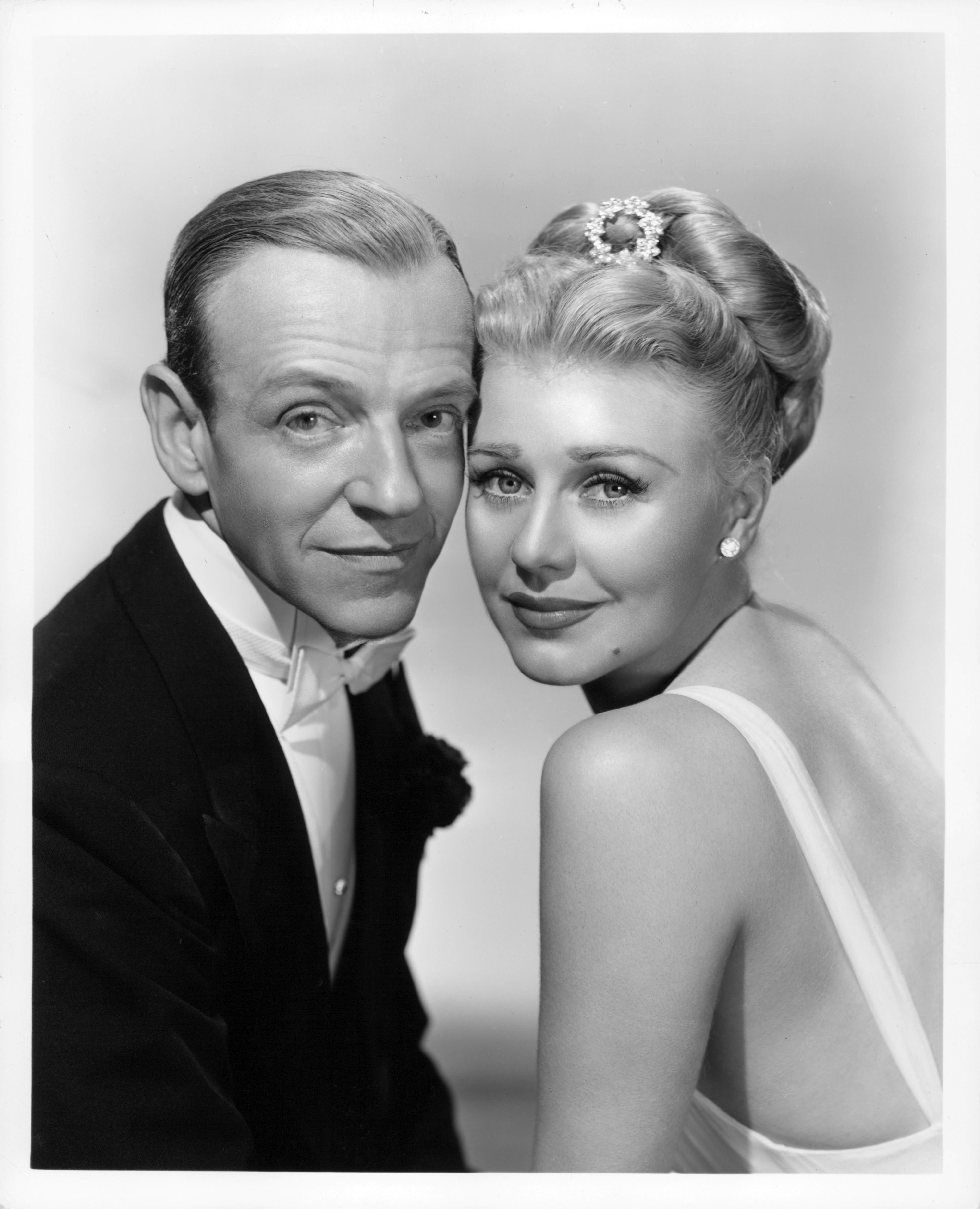 Two classic film stars smiling closely, man in tuxedo, woman with elegant hairdo