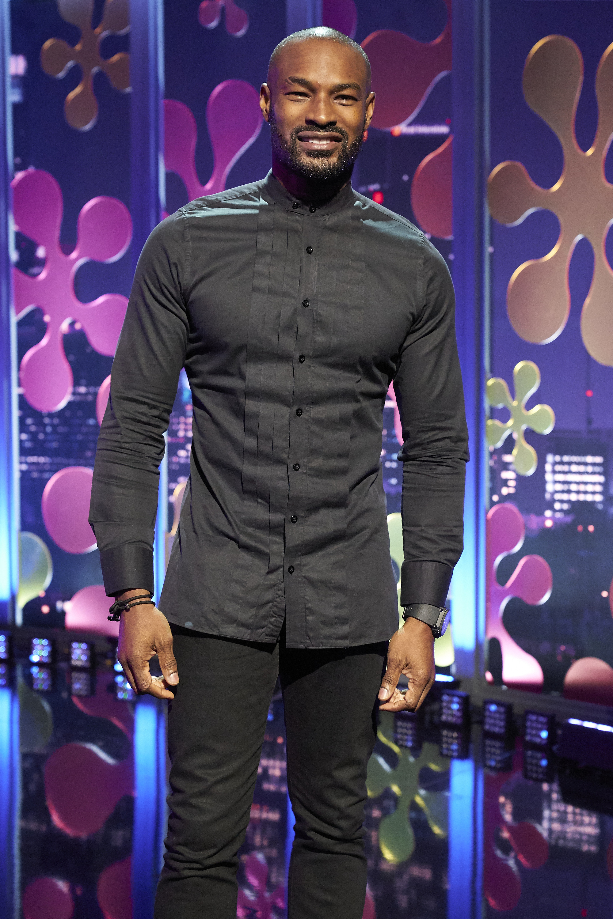 Tyson Beckford posing in a sleek black button-up shirt and matching trousers