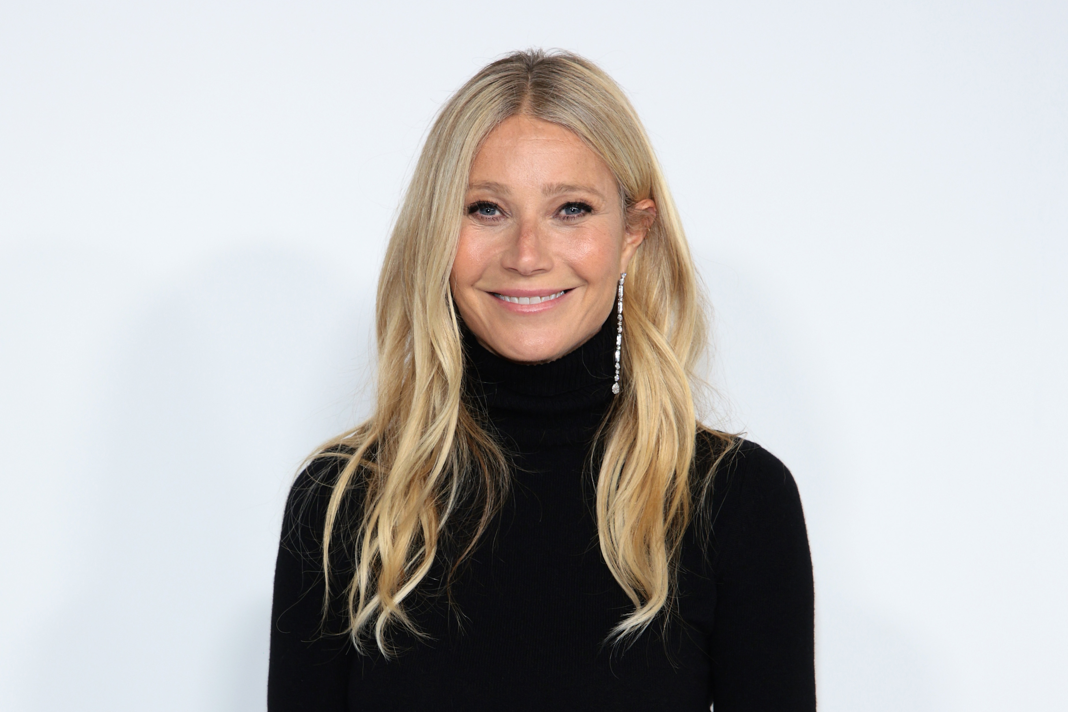 Gwyneth Paltrow smiling in a black turtleneck, with her hair down and long earrings