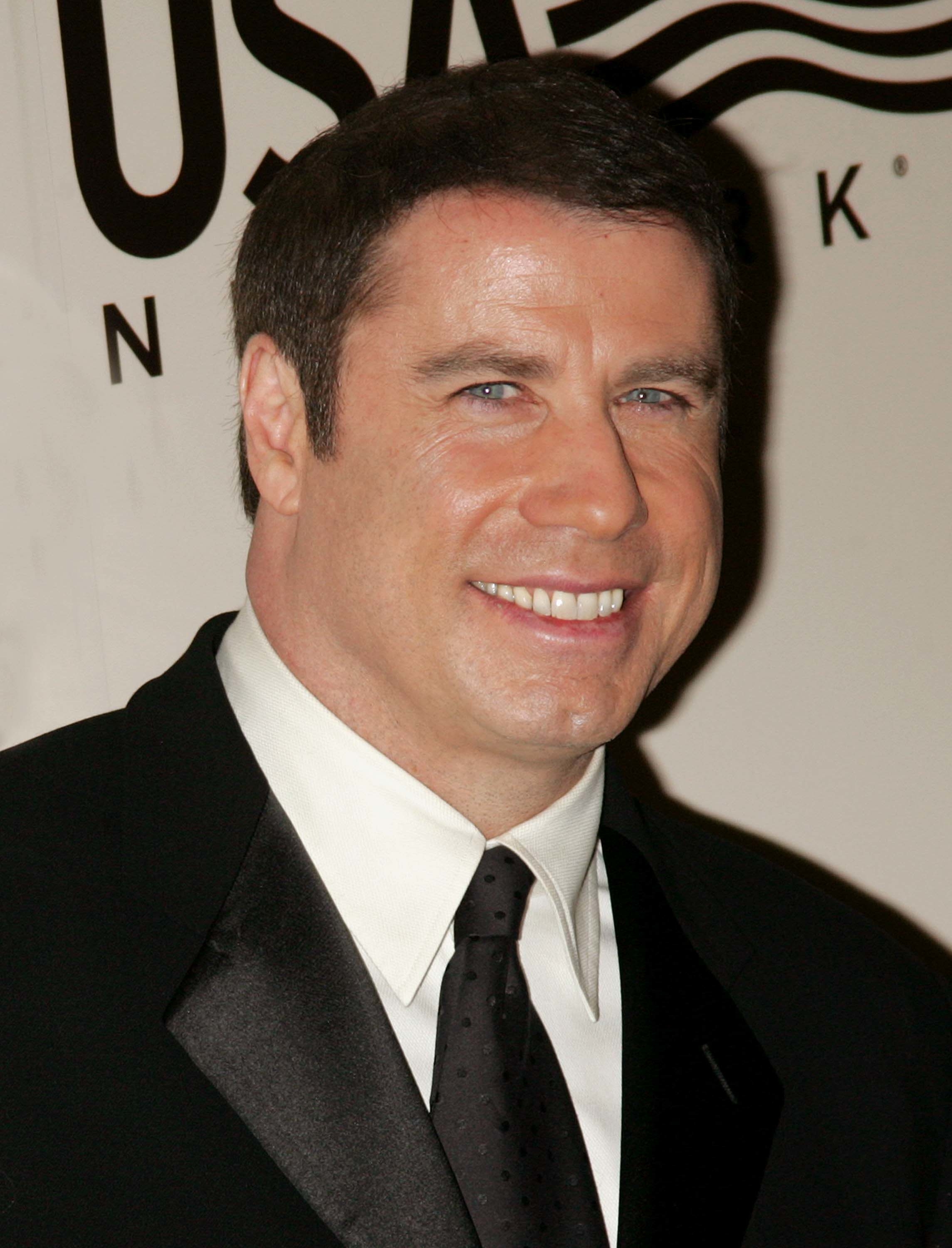 John Travolta smiling in a black suit at a USA Network event