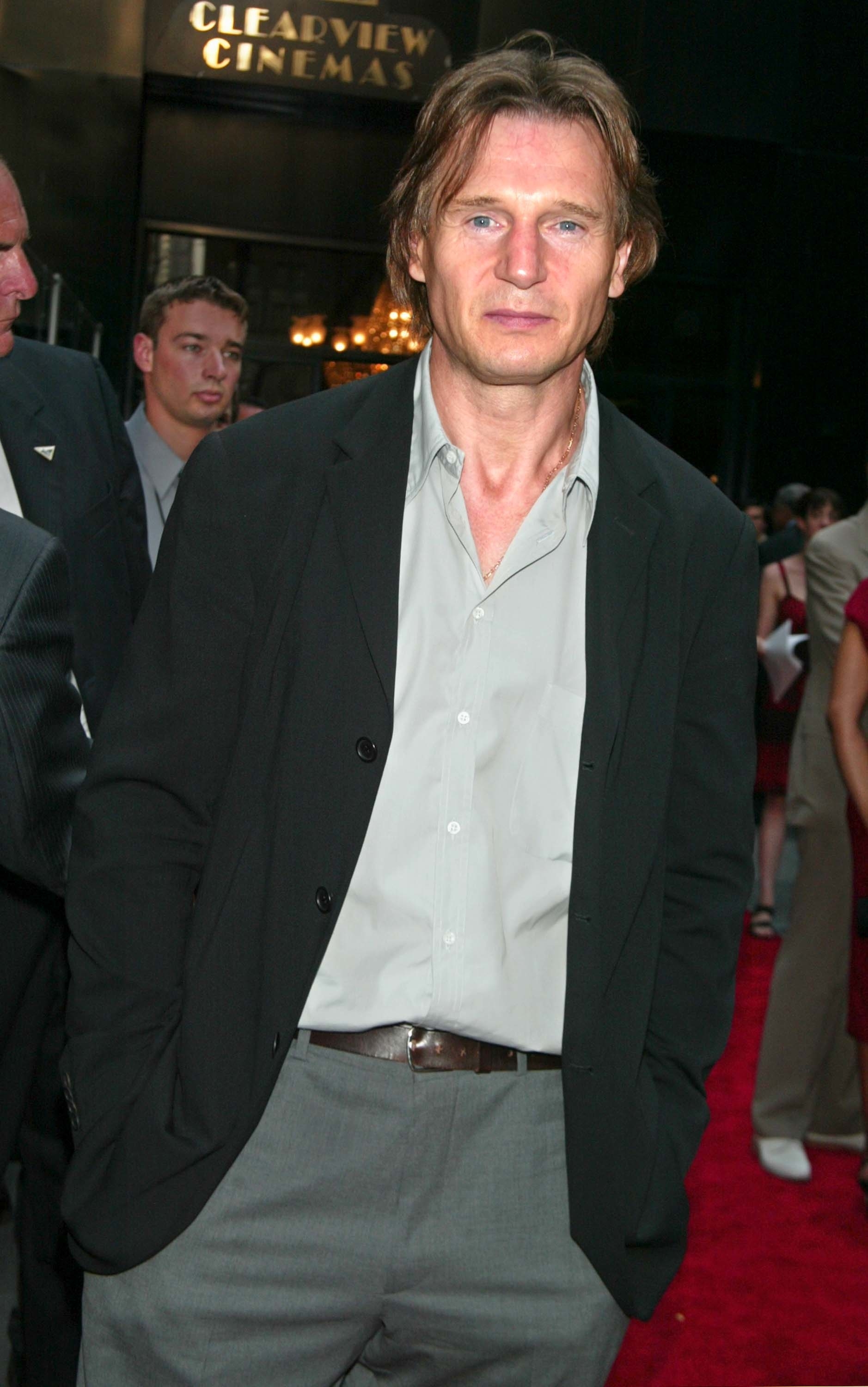 Man in a black blazer and open-collar shirt at a premiere event