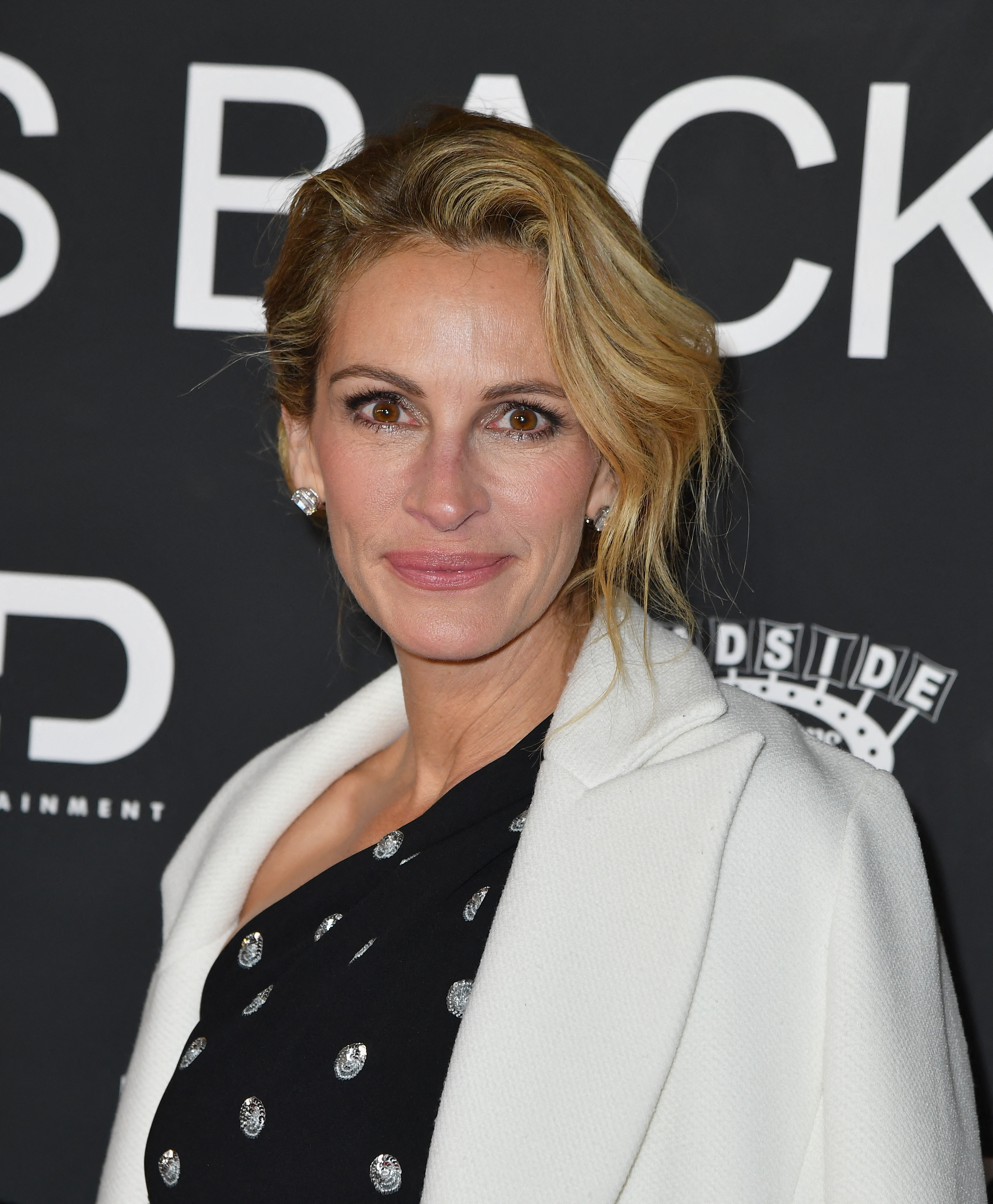 Woman with updo and white blazer over a black dress adorned with crystals, posing at an event