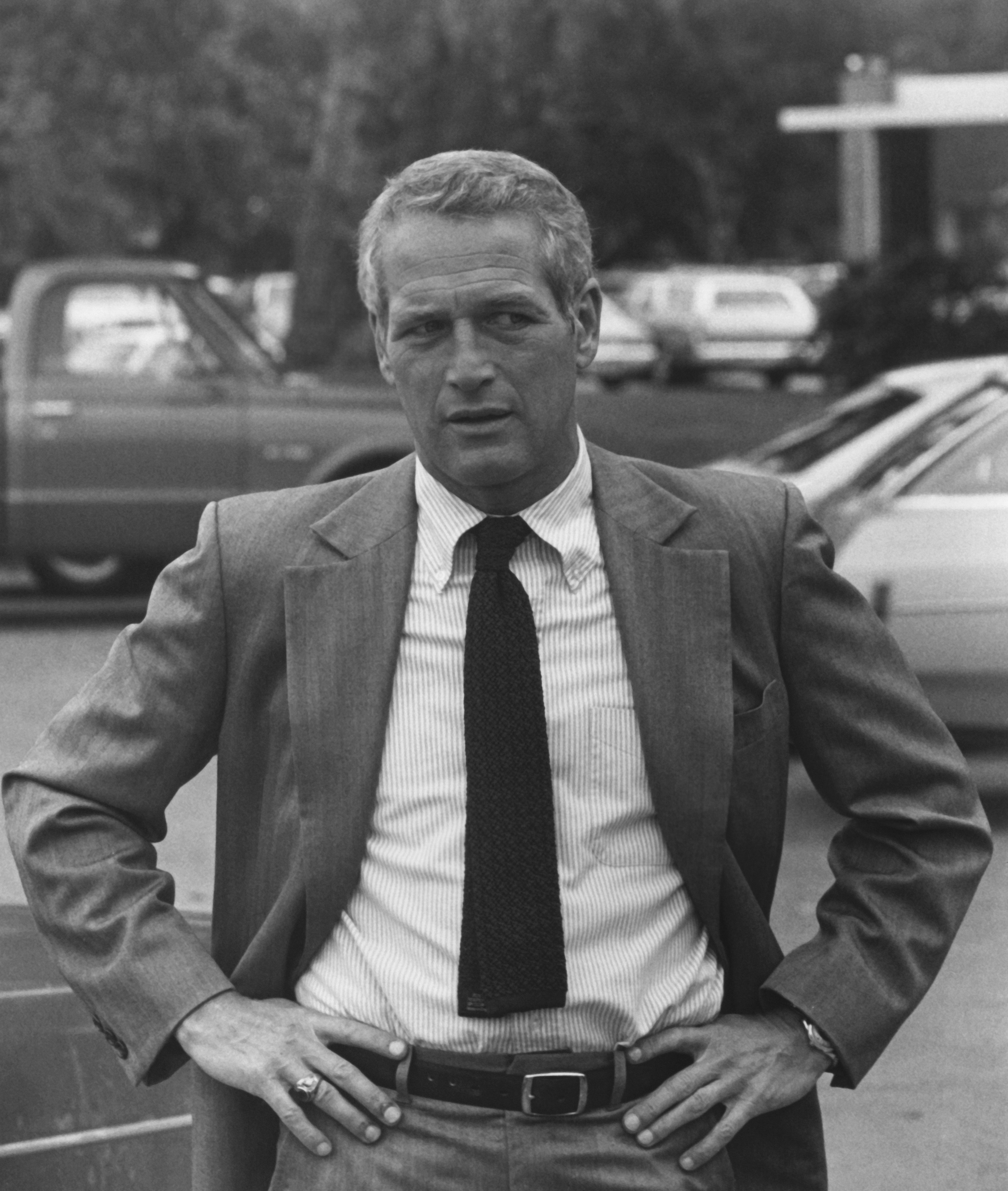 Man in suit with hands on hips standing in front of cars