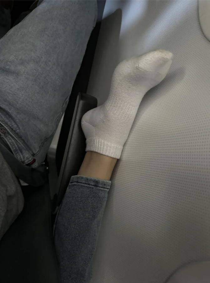 Person&#x27;s foot in a white sock resting on an airplane seat divider