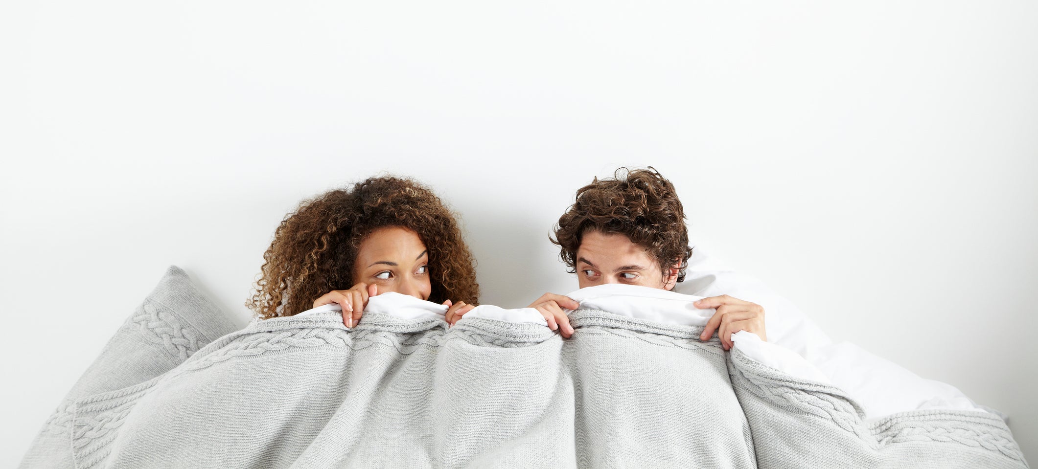 Two people peeking over a blanket with playful expressions