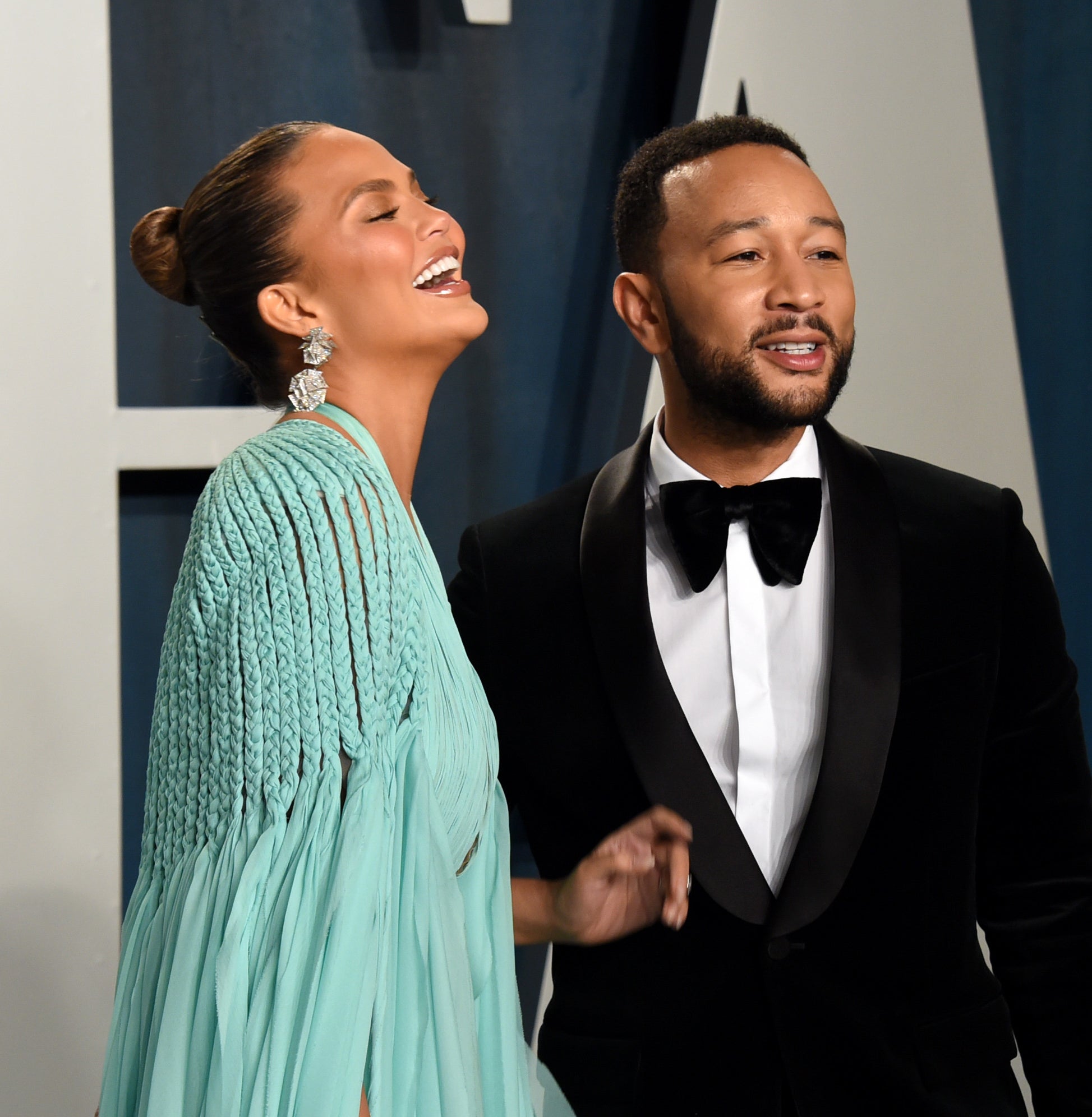 Chrissy Teigen in a pleated dress laughs with John Legend in a classic tuxedo