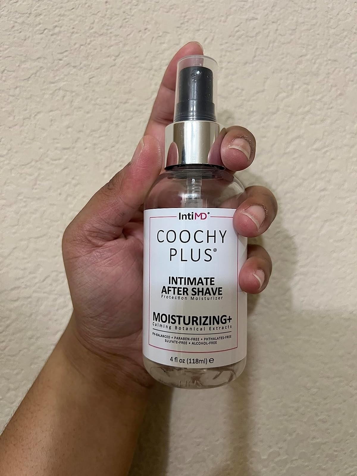Hand holding IntiMD Coochy Plus Intimate Moisturizing After Shave in a clear bottle with white label