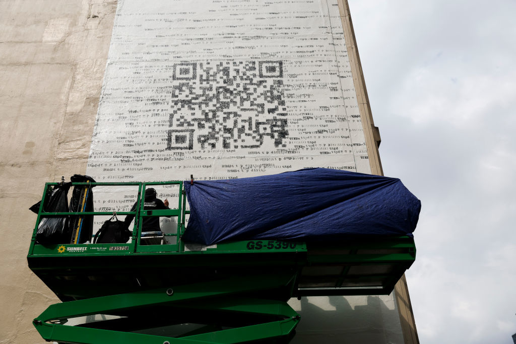 Large QR code mural on a building wall with a covered scissor lift in front