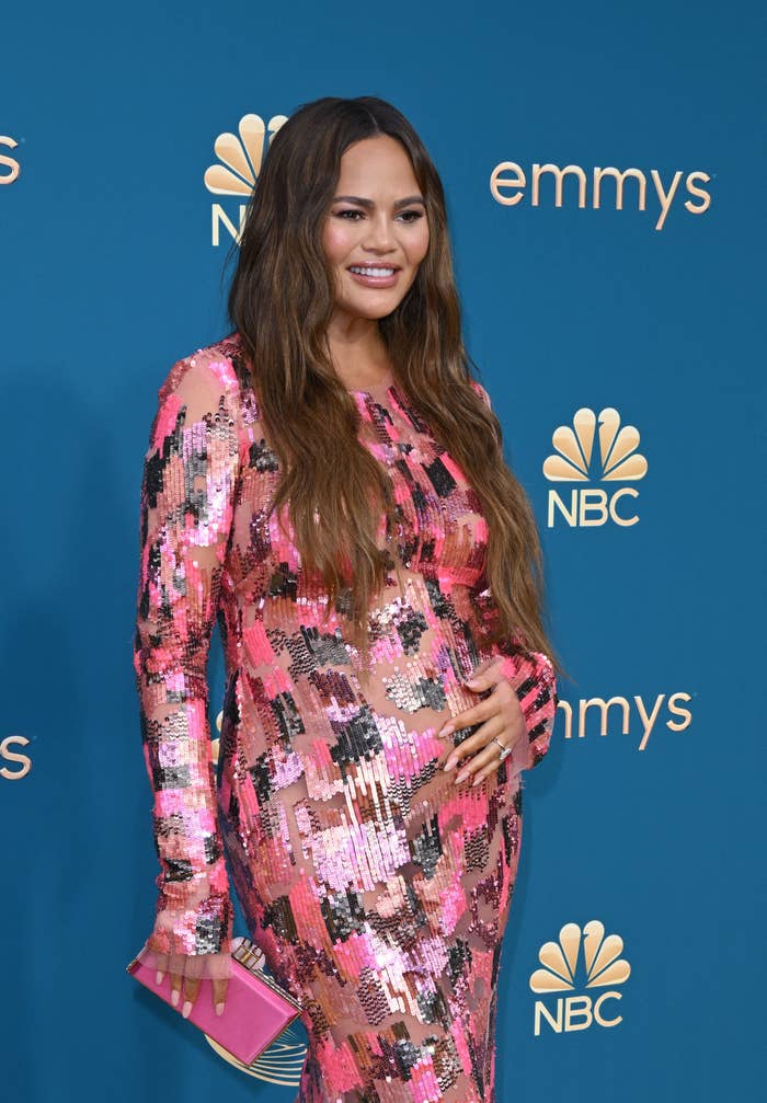 Chrissy Teigen posing in a shimmering, sequined dress at the Emmy Awards holding her baby bump