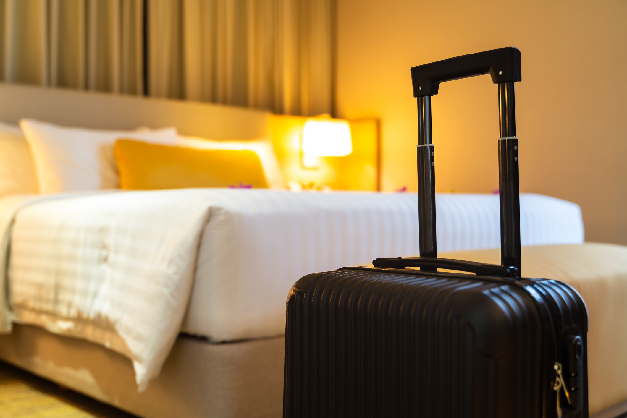 A suitcase in the foreground with an unfocused hotel room bed in the background, suggesting travel for work