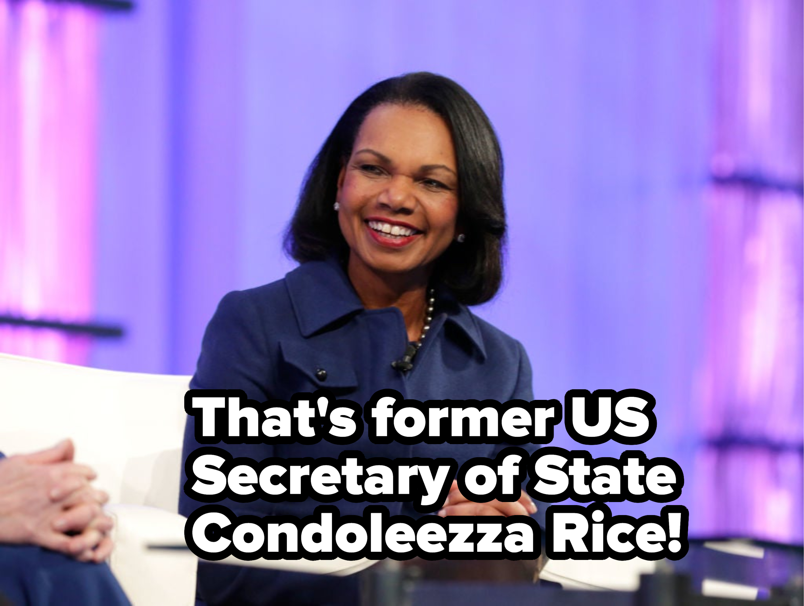 Condoleezza Rice seated in an interview setting, smiling, wearing a dark peacoat