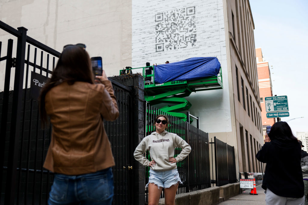 Person in a hoodie and shorts stands by a large QR code mural as others take photos