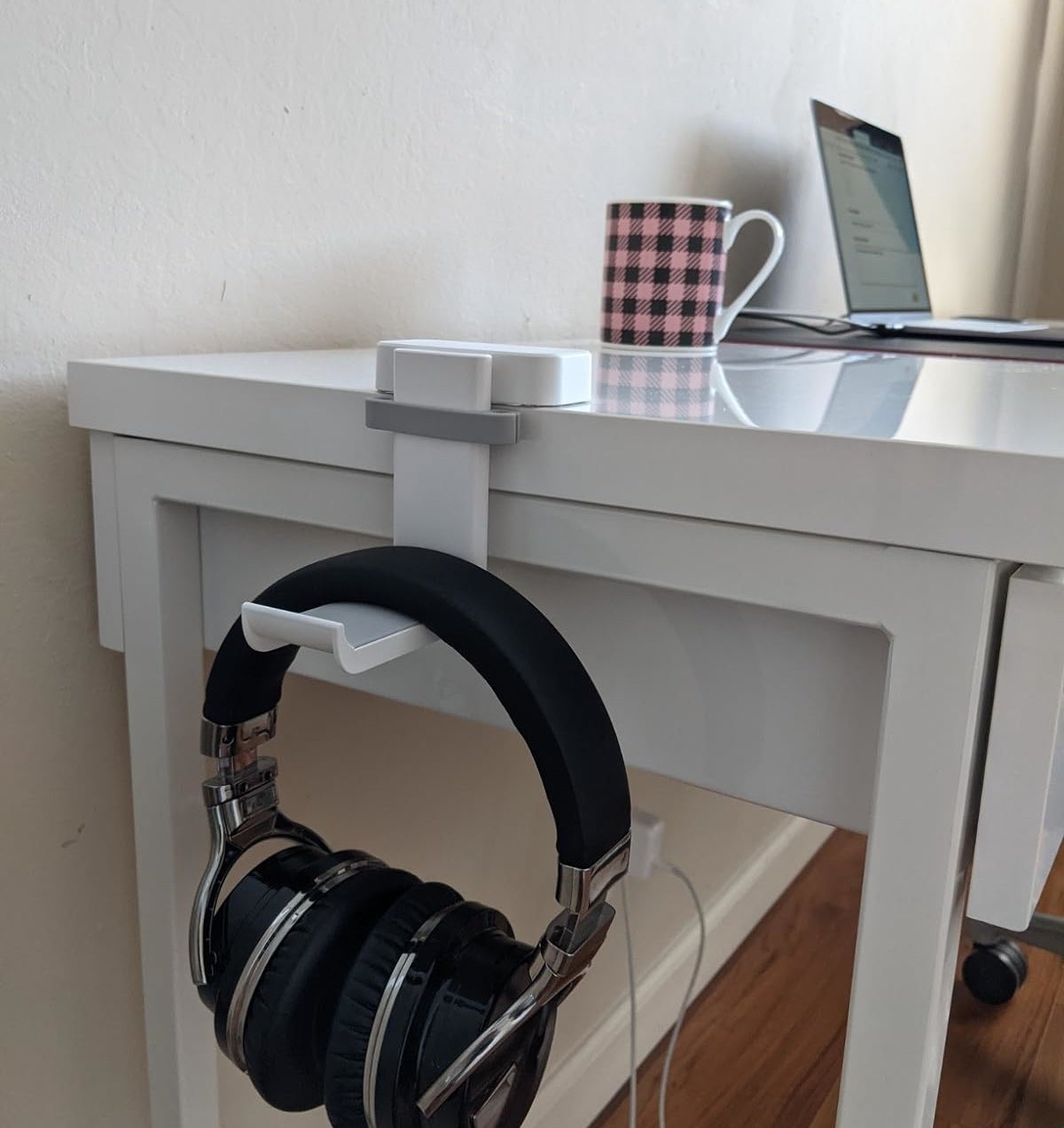 Headphones hanging on a desk edge near a checkered mug and a laptop partially visible