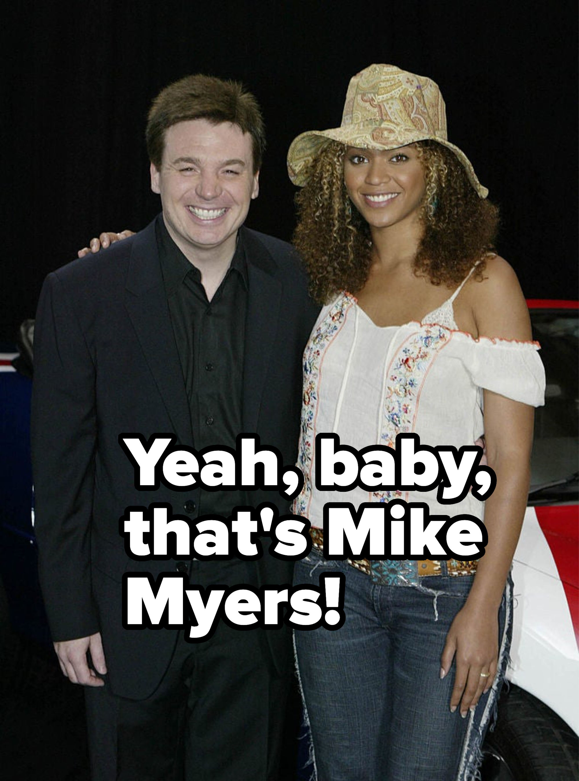 Man in a suit and woman in a hat and blouse smiling next to a car
