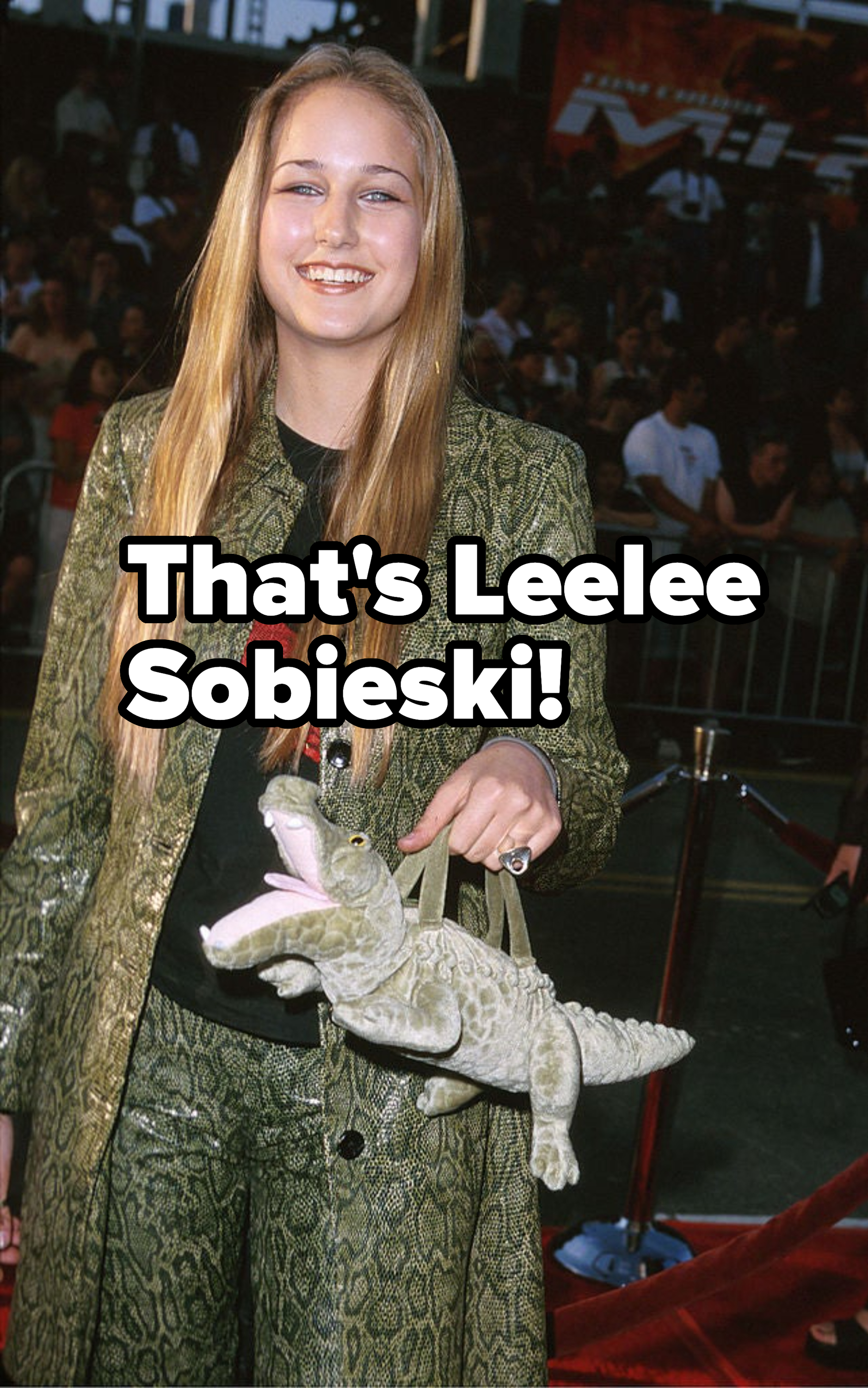 Person smiling with long straight hair, in a textured jacket, holding a toy dinosaur at an event