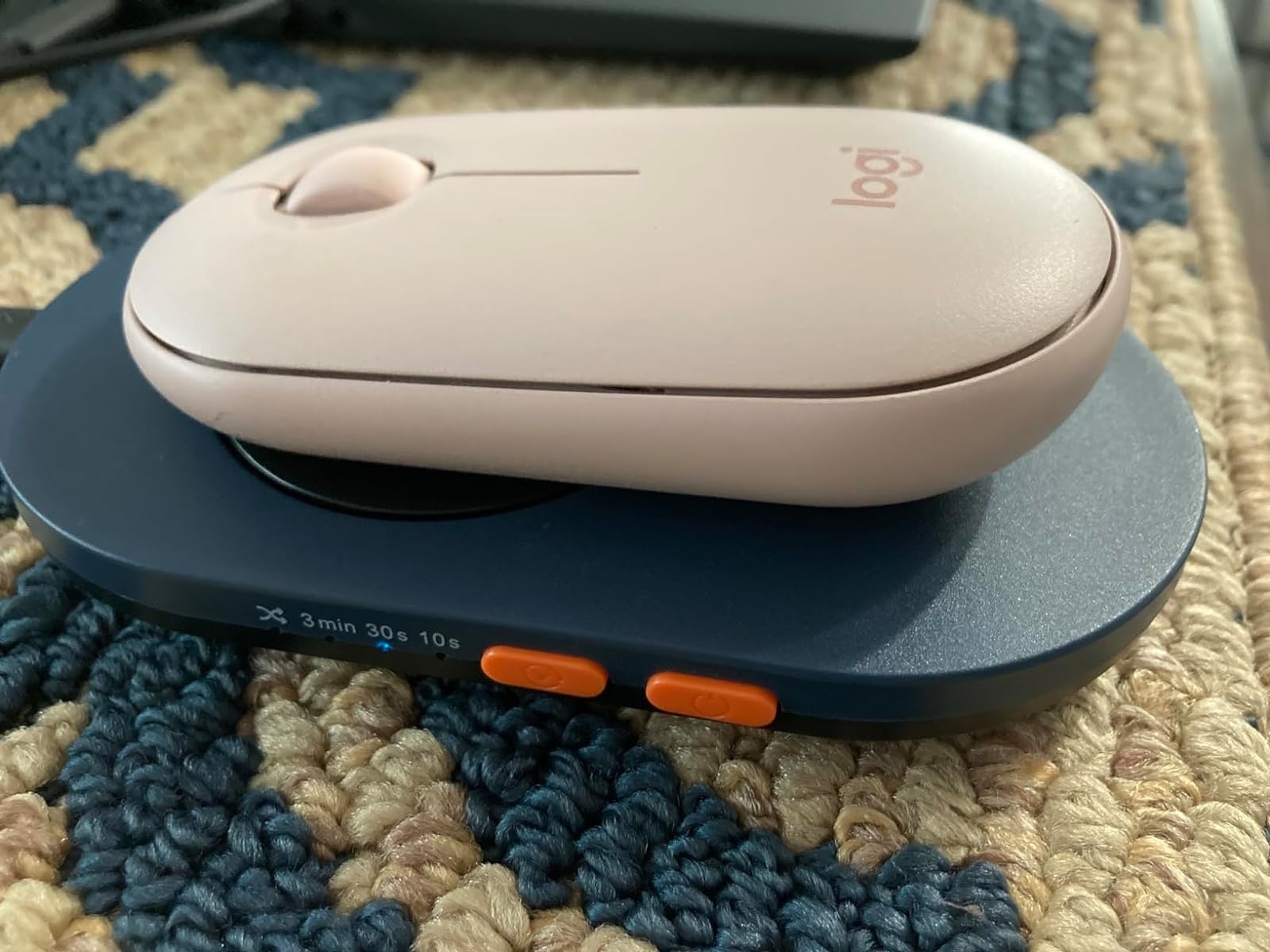 A wireless mouse on a charging pad placed on a woven surface