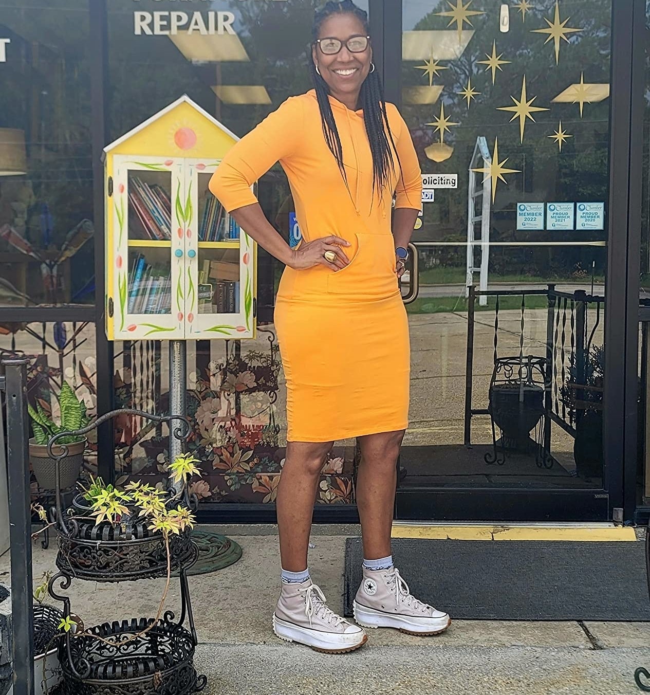Reviewer&#x27;s photo of them wearing the hoodie dress in the color orange, styled with white high top sneakers