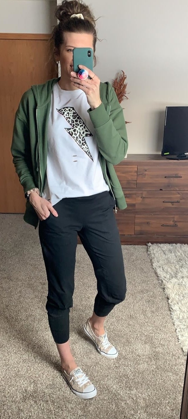 Reviewer&#x27;s photo of them wearing the joggers in the color black, styled with a white and black graphic tee, an unzipped green hoodie, and white Converse low-tops, taking a mirror selfie with a phone