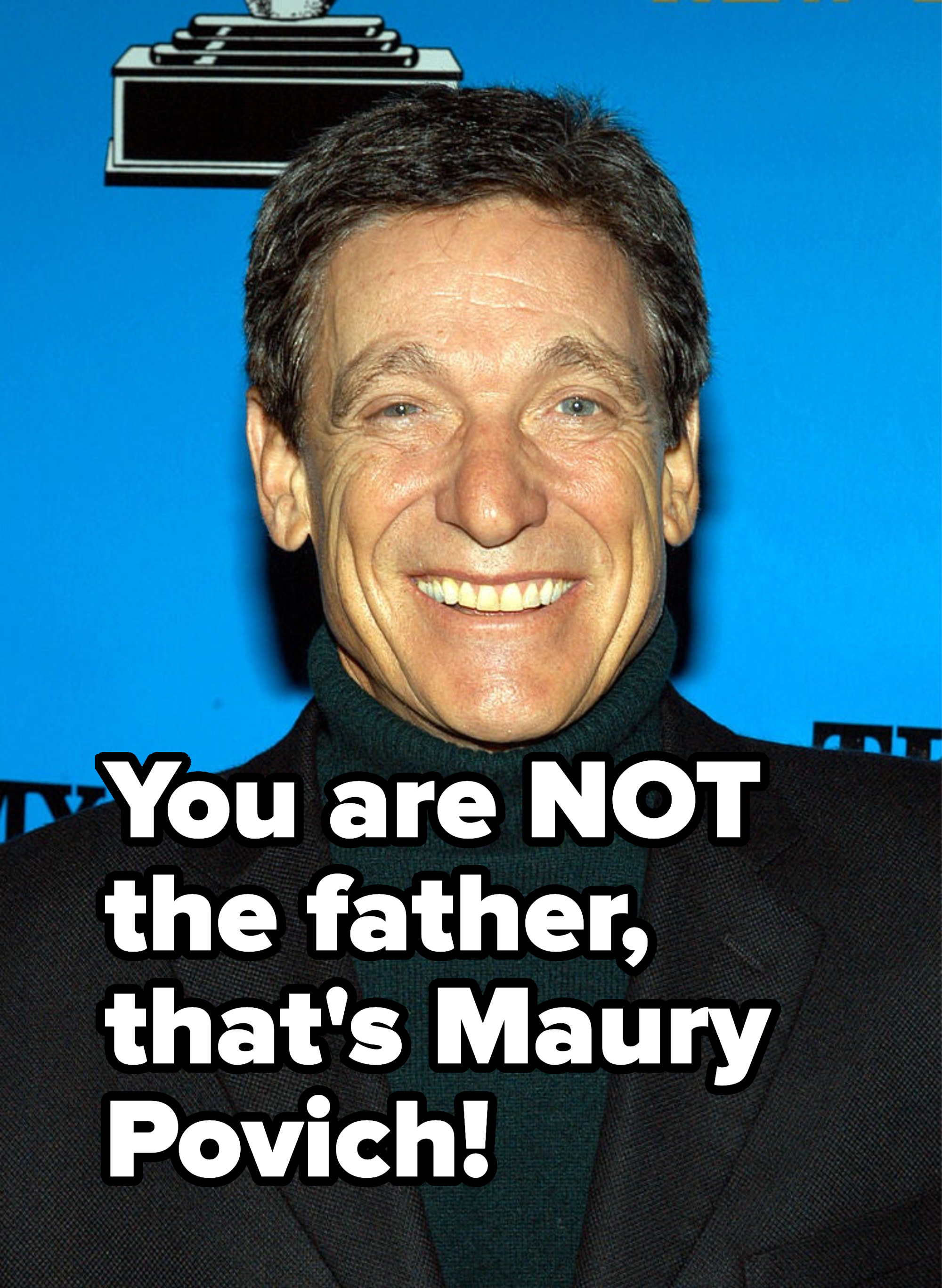 Man in a turtleneck and blazer smiling at a media event