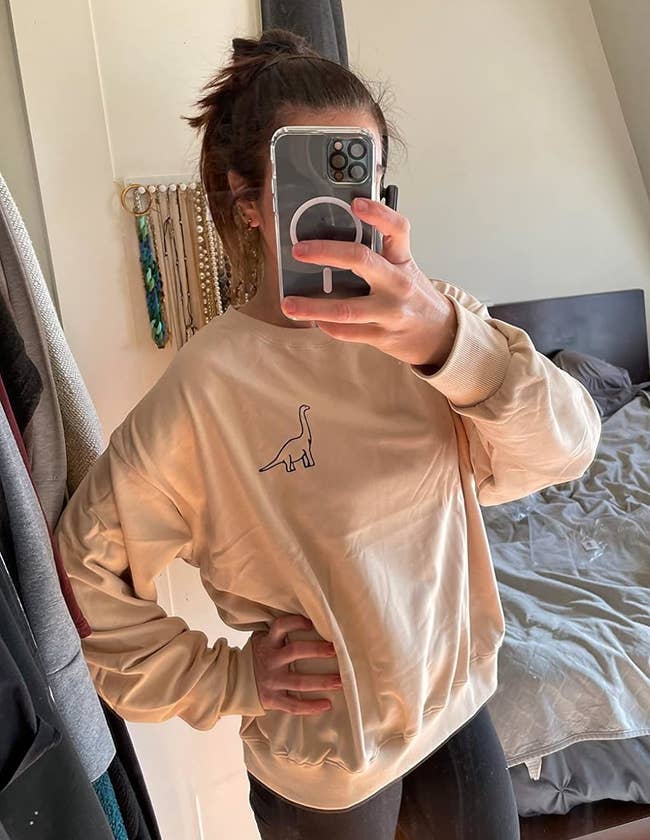 Reviewer's photograph of them wearing the sweatshirt successful the colour apricot styled with achromatic leggings, taking a reflector selfie with a phone