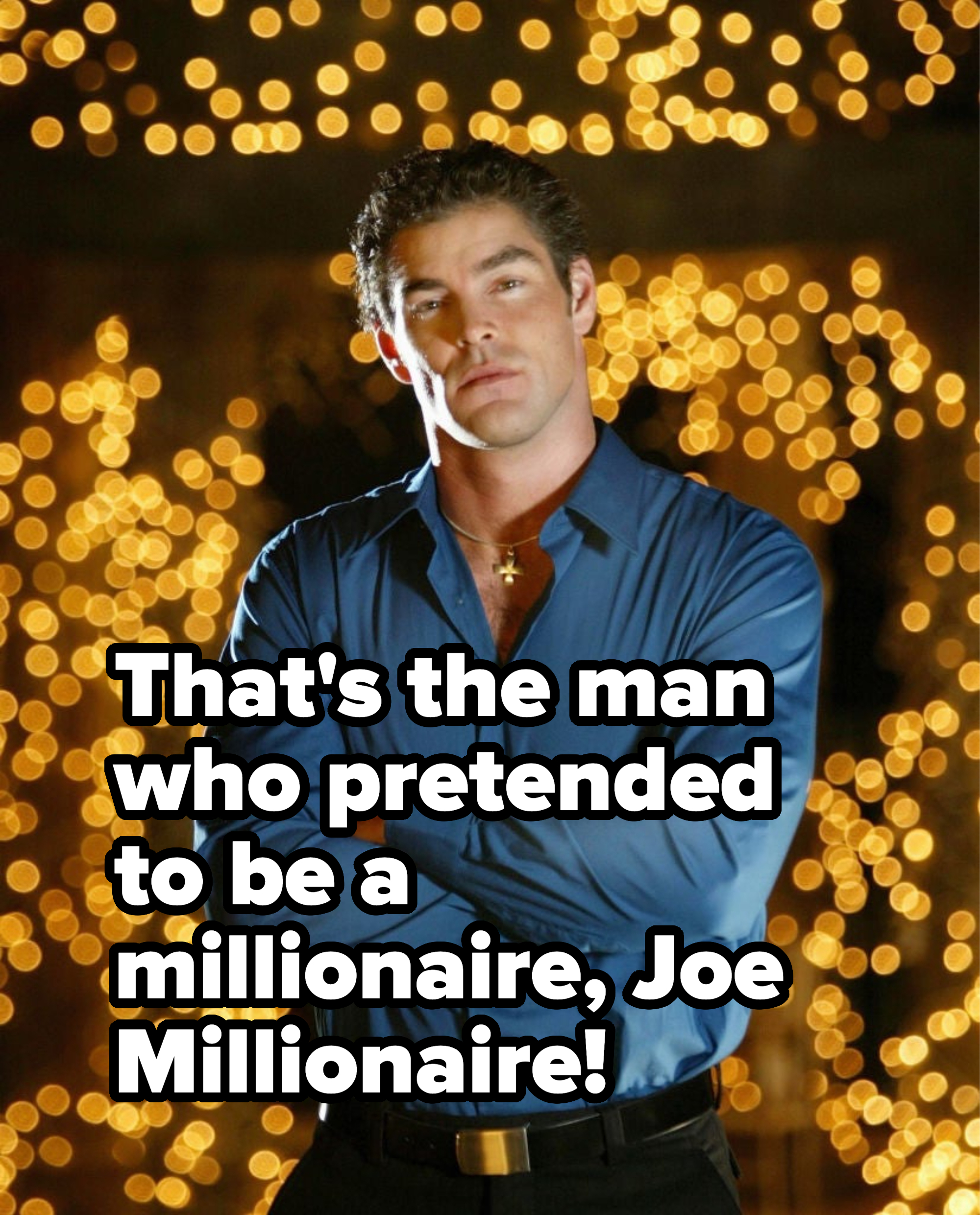 Man in a satin blue shirt and black trousers posing with arms crossed, bokeh lights in background