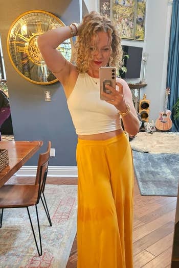 Reviewer's photograph of them wearing a achromatic cropped tank, styled with wide limb yellowish pants
