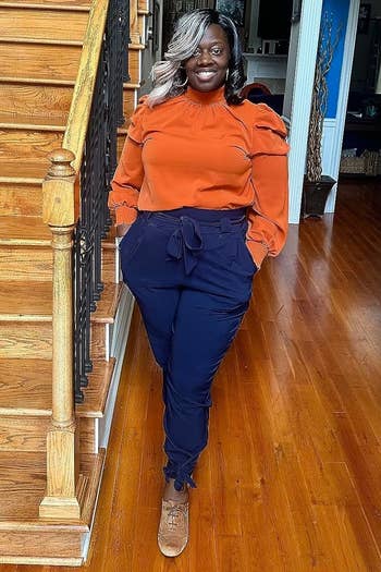 Reviewer's photograph of them wearing the pencil pants successful the colour blue, styled with an orangish high-neck agelong sleeved apical and golden sneakers