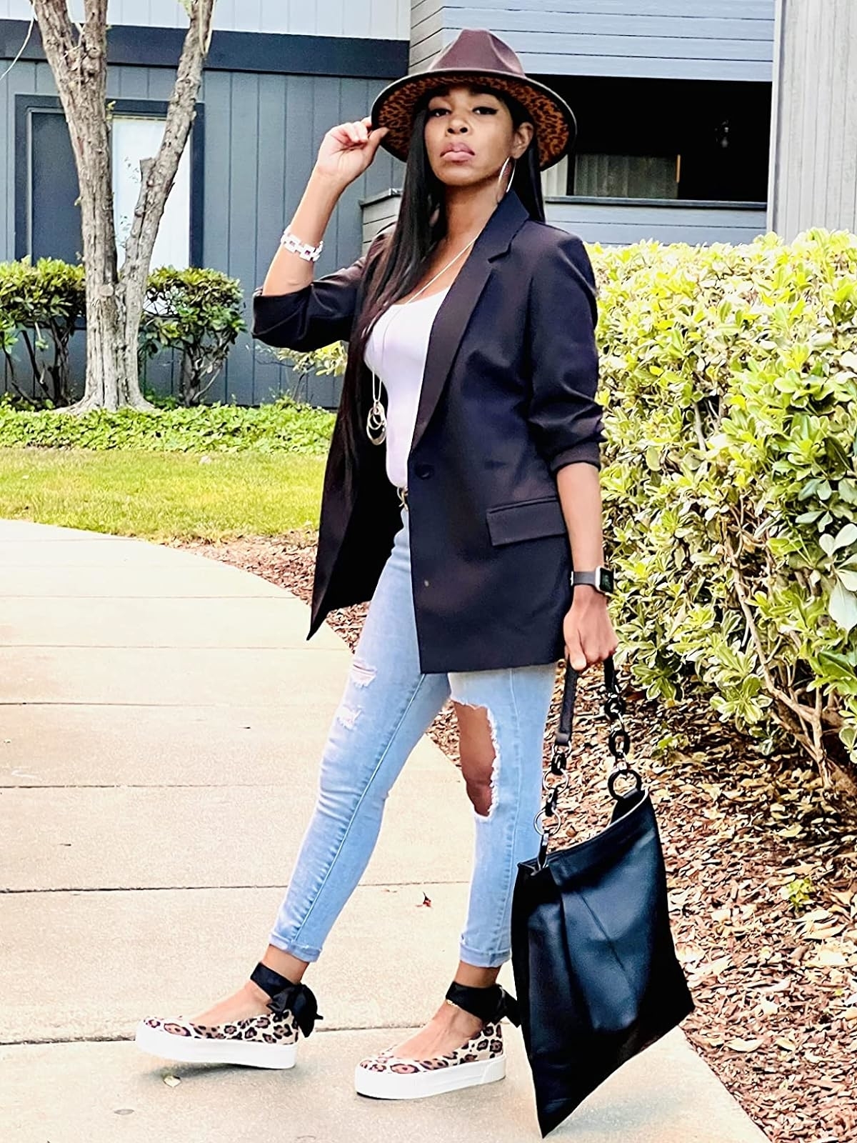 Reviewer&#x27;s photo of them wearing the blazer in the color black, styled with skinny jeans, a white tee, a black handbag, leopard print sneaker flats, and a brown fedora
