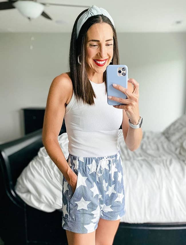Reviewer's photograph of them wearing bluish shorts with a achromatic prima pattern, styled with a achromatic vessel top, taking a reflector selfie with a phone