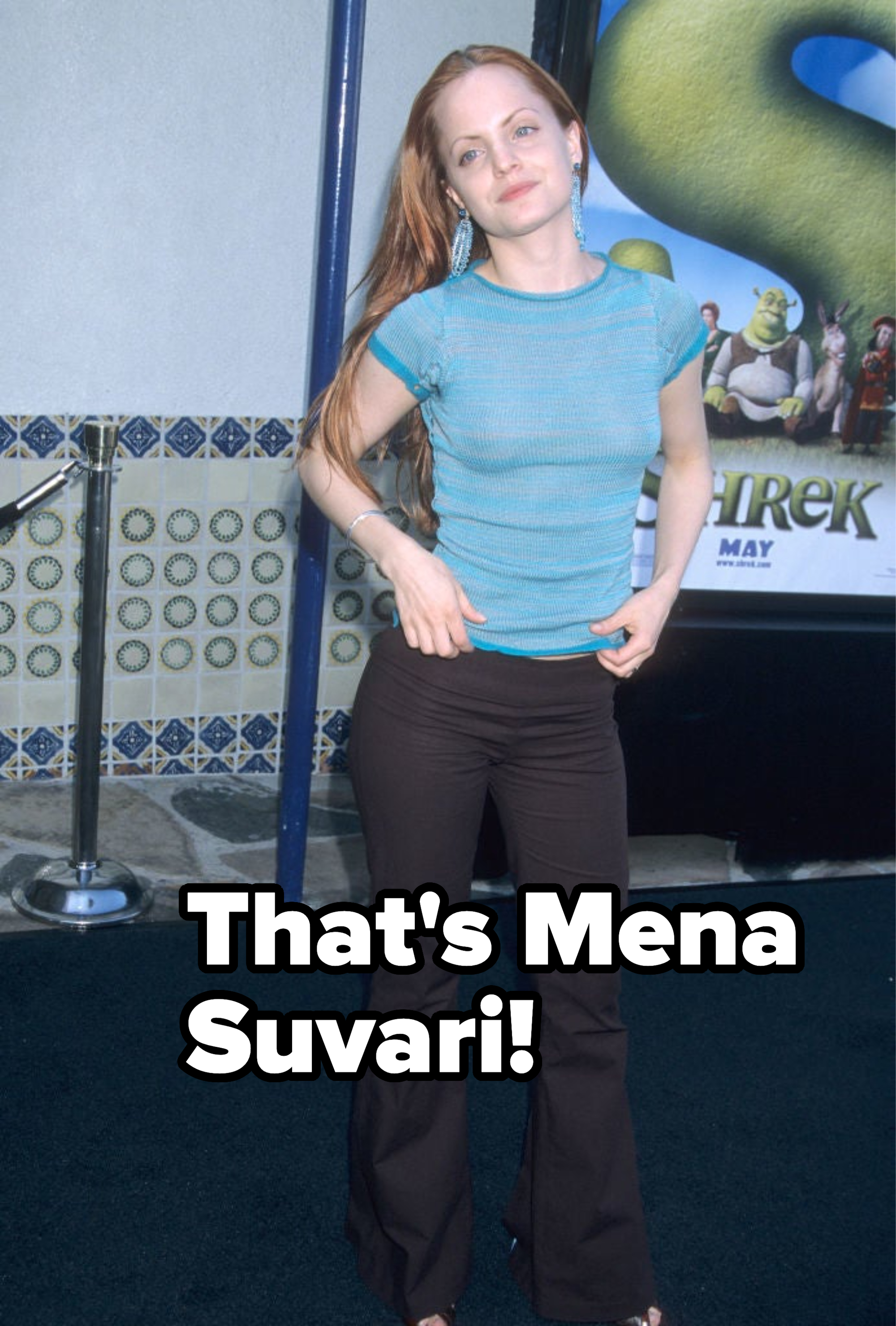 Woman in casual blue top and brown pants posing with hand on hip