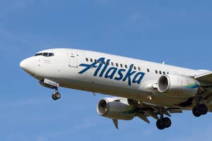 Alaska Airlines aircraft mid-flight with landing gear down, clear sky in the background