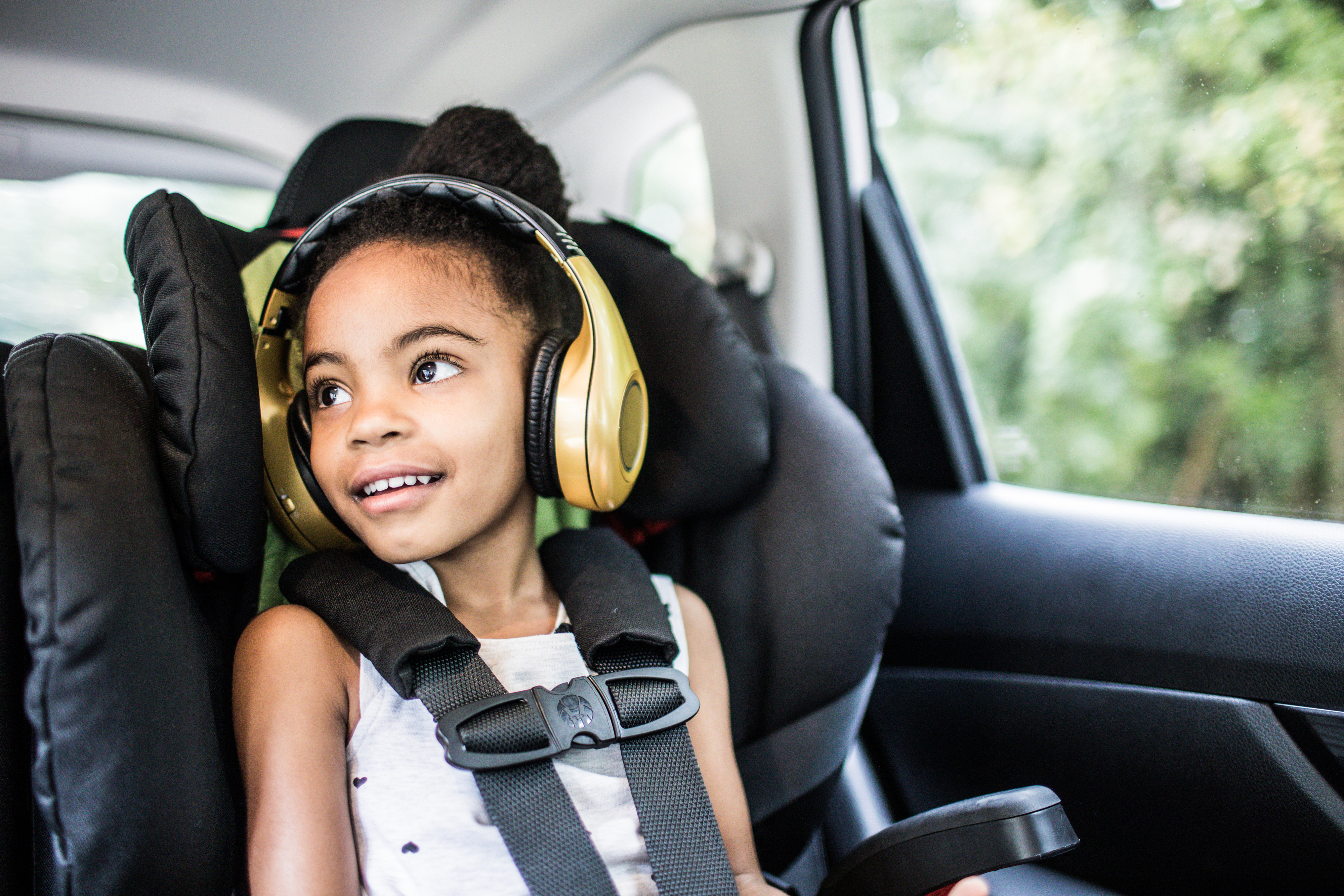 Young child in car seat wearing headphones, looking out window, possibly during a commute