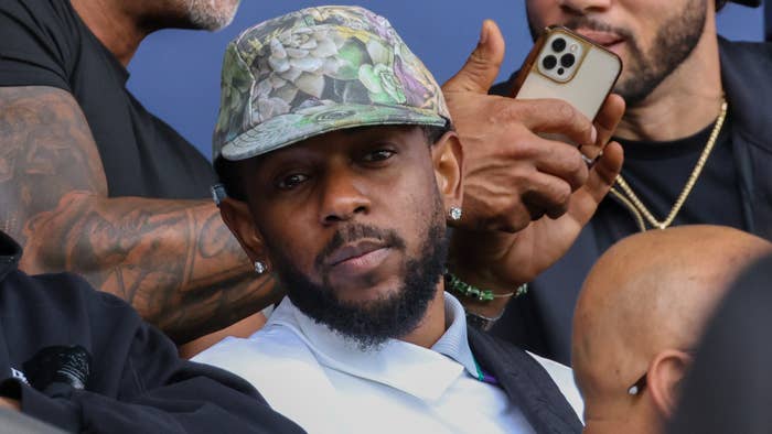 Music artist in a bucket hat, surrounded by people, one holding a smartphone