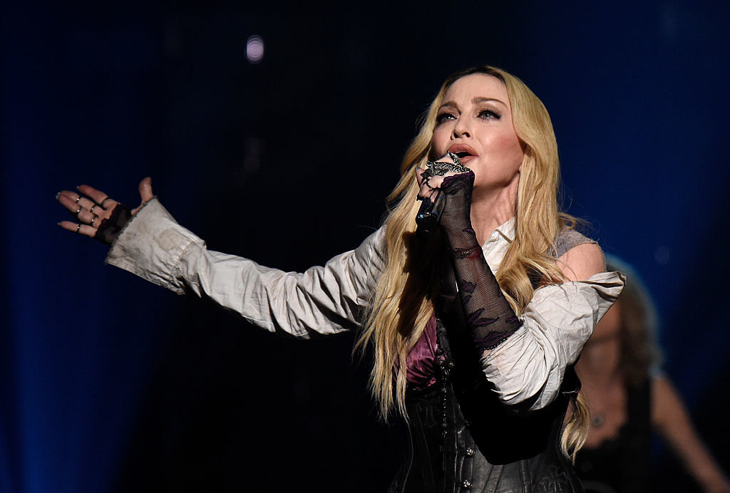 Madonna performing on stage in a layered outfit with a corset and gloves