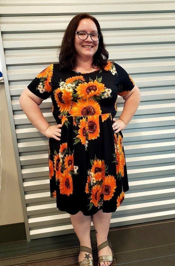 Reviewer&#x27;s photo of them wearing the dress in the sunflower pattern, styled with gold sandals