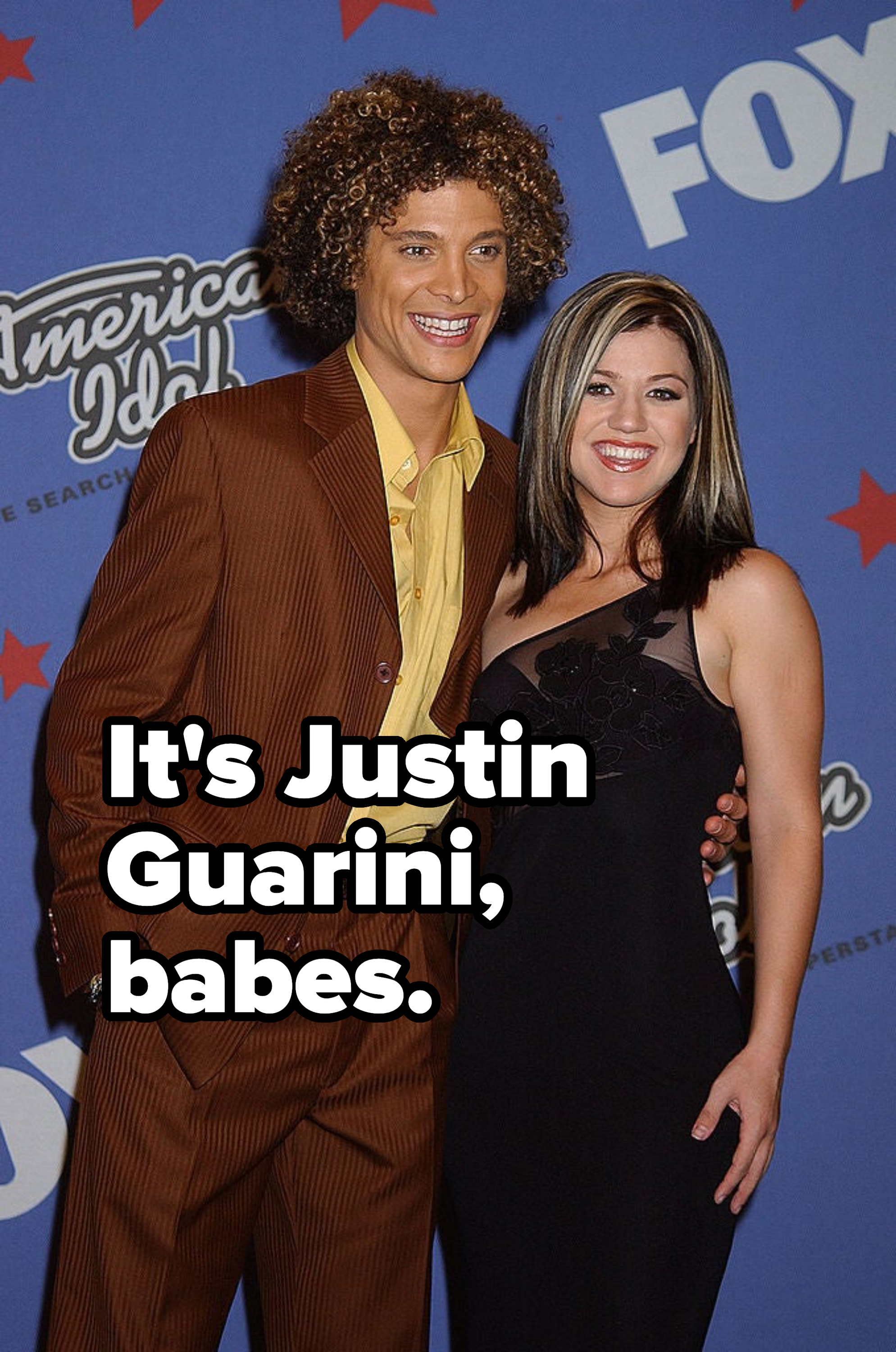 Two people posing on the red carpet, one in a striped suit with a yellow shirt, the other in a black dress with lace detail