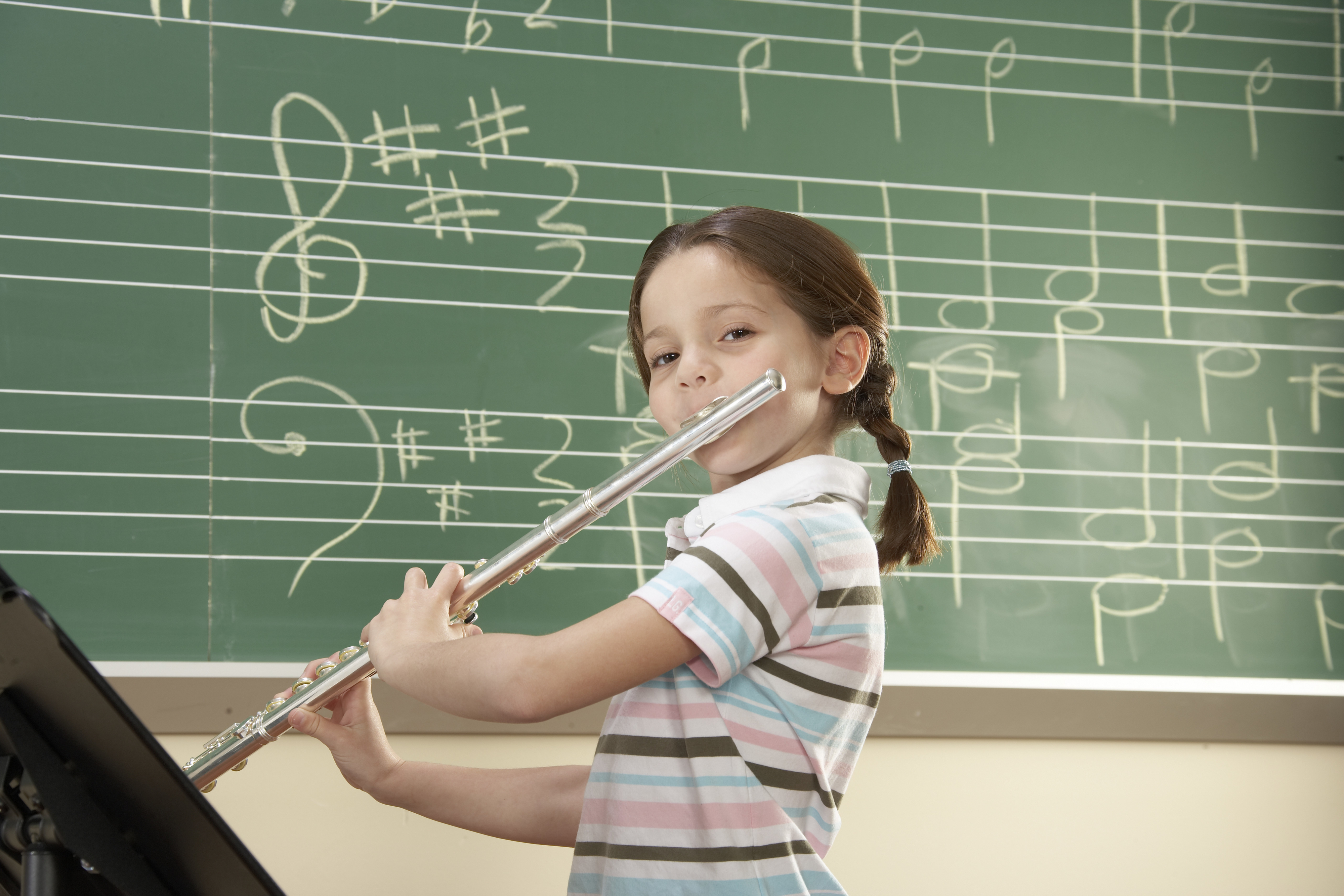 Young student playing flute in music class with chalkboard notation in background